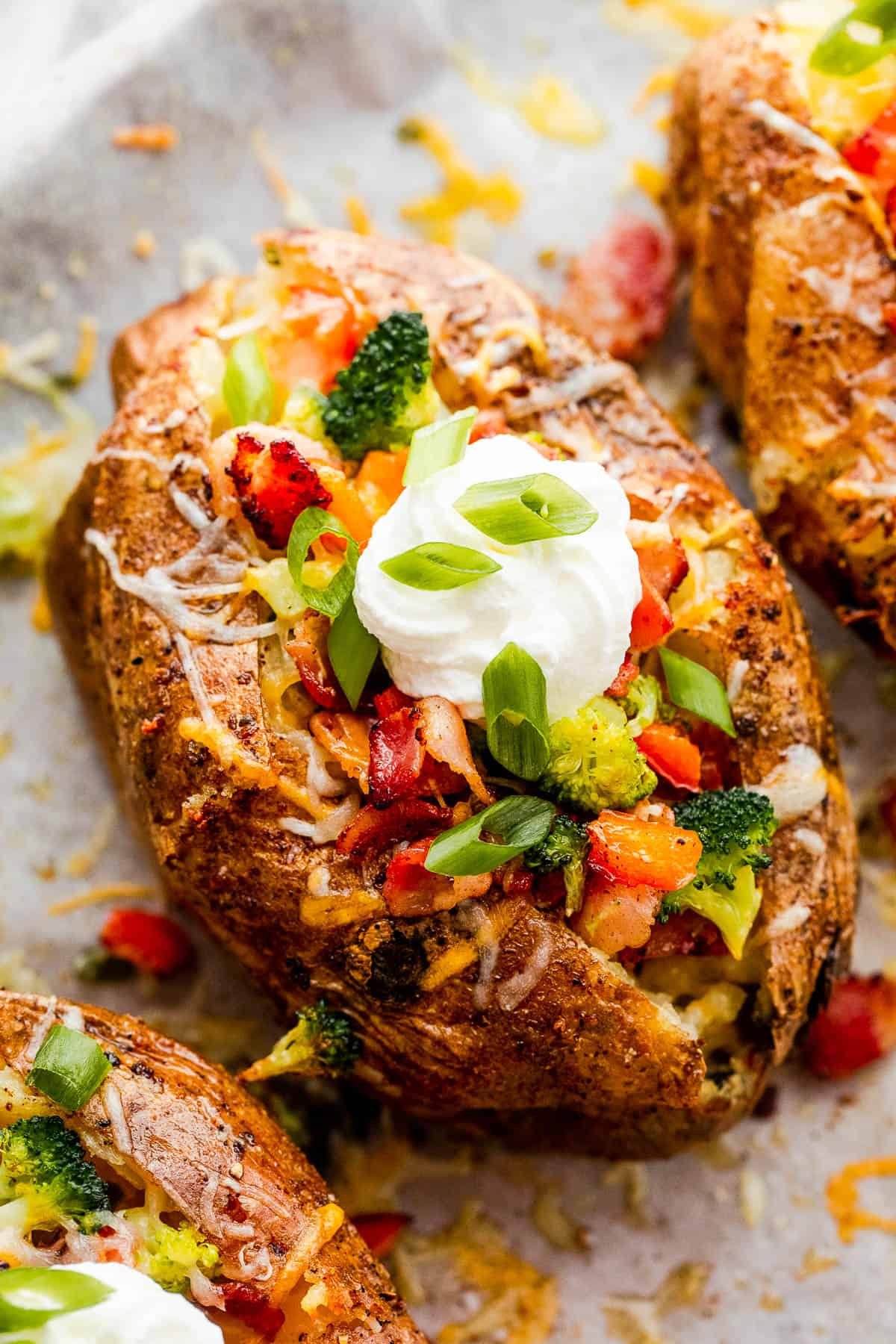 Three Instant Pot Baked Potatoes Beside Bowls of Cheese, Broccoli, Bacon, Chopped Green Onions and Sour Cream