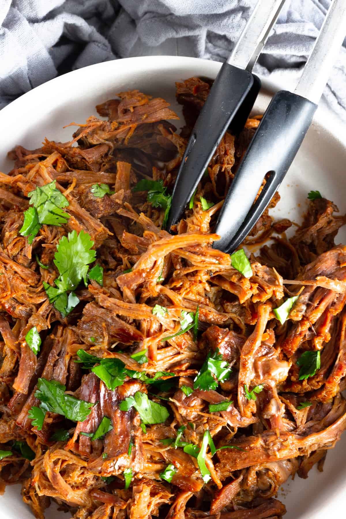 A White Bowl Containing Juicy Beef Barbacoa with Some Fresh Parsley on Top