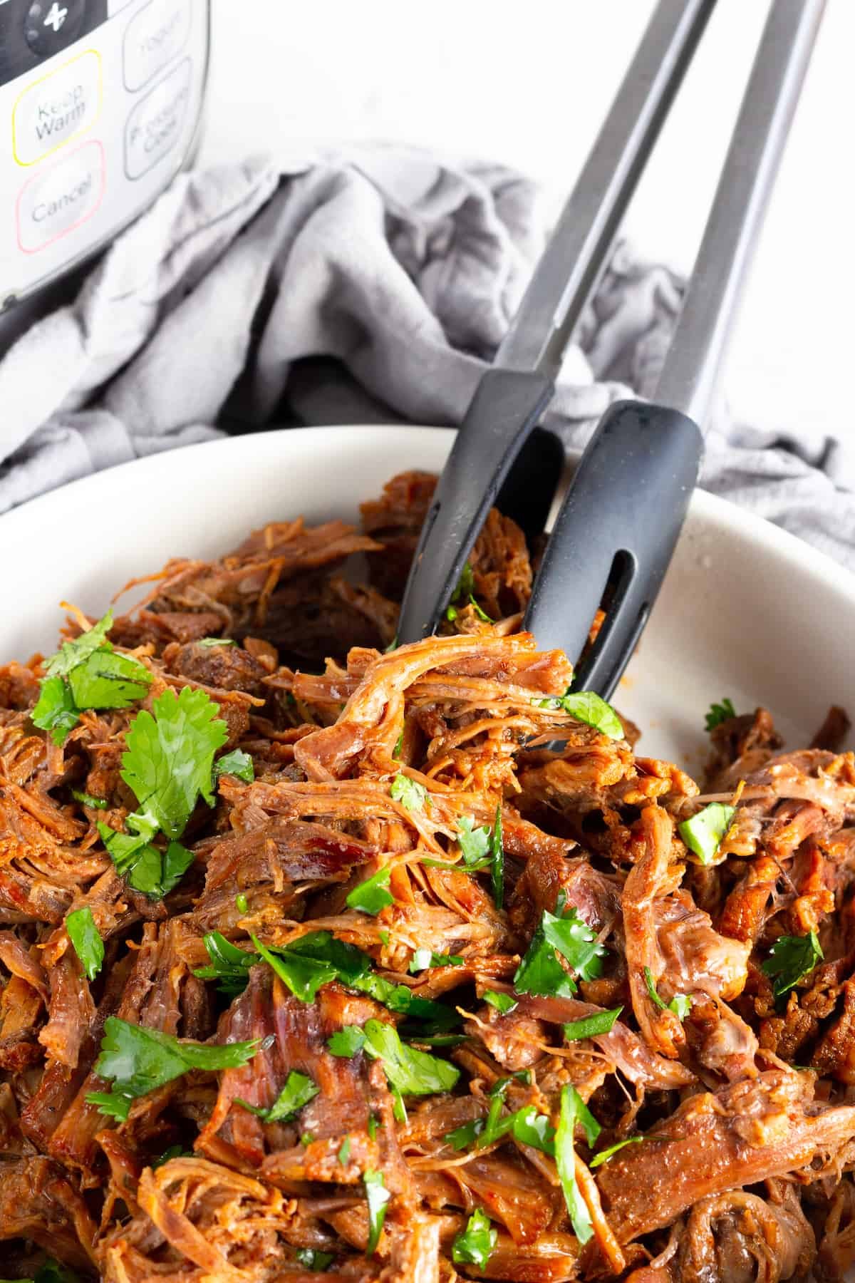 A Pair of Metal Tongs Digging Into a Bowl of Instant Pot Beef