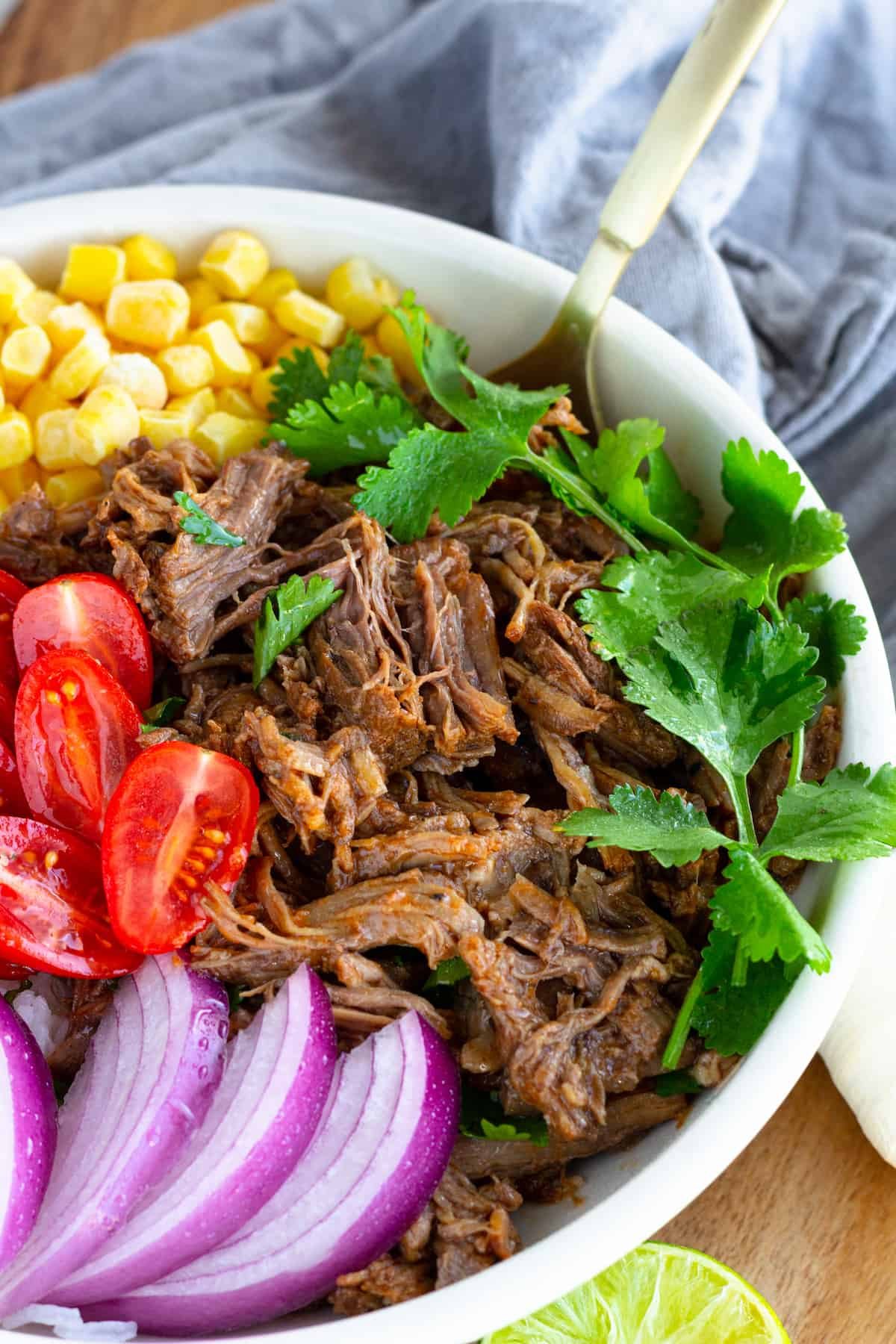 A Beef Barbacoa Burrito Bowl with a Parsley Garnish and a Golden Spoon Inside