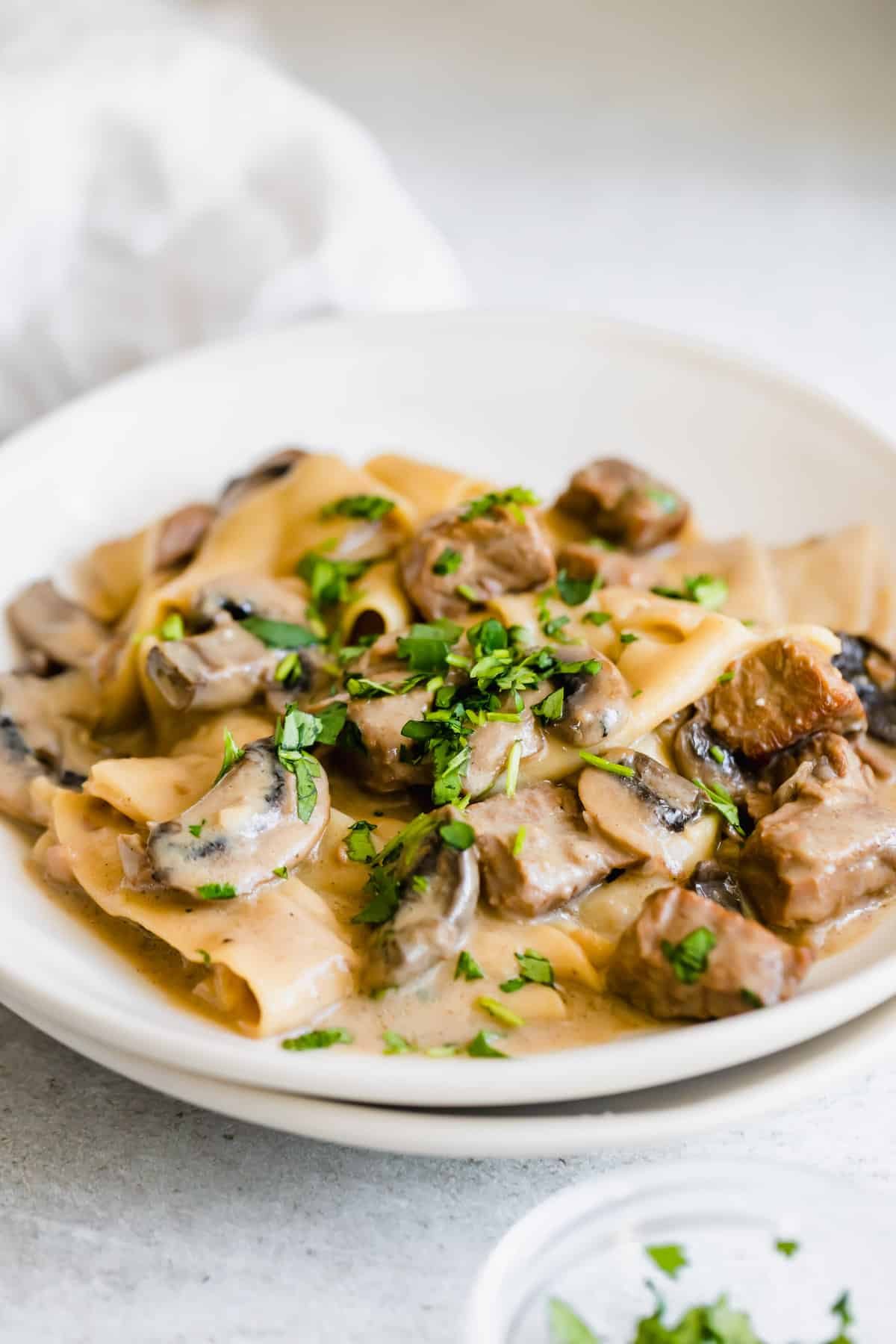 A Plate of Beef Stroganoff Next to a Small Bowl of Chopped Parsley