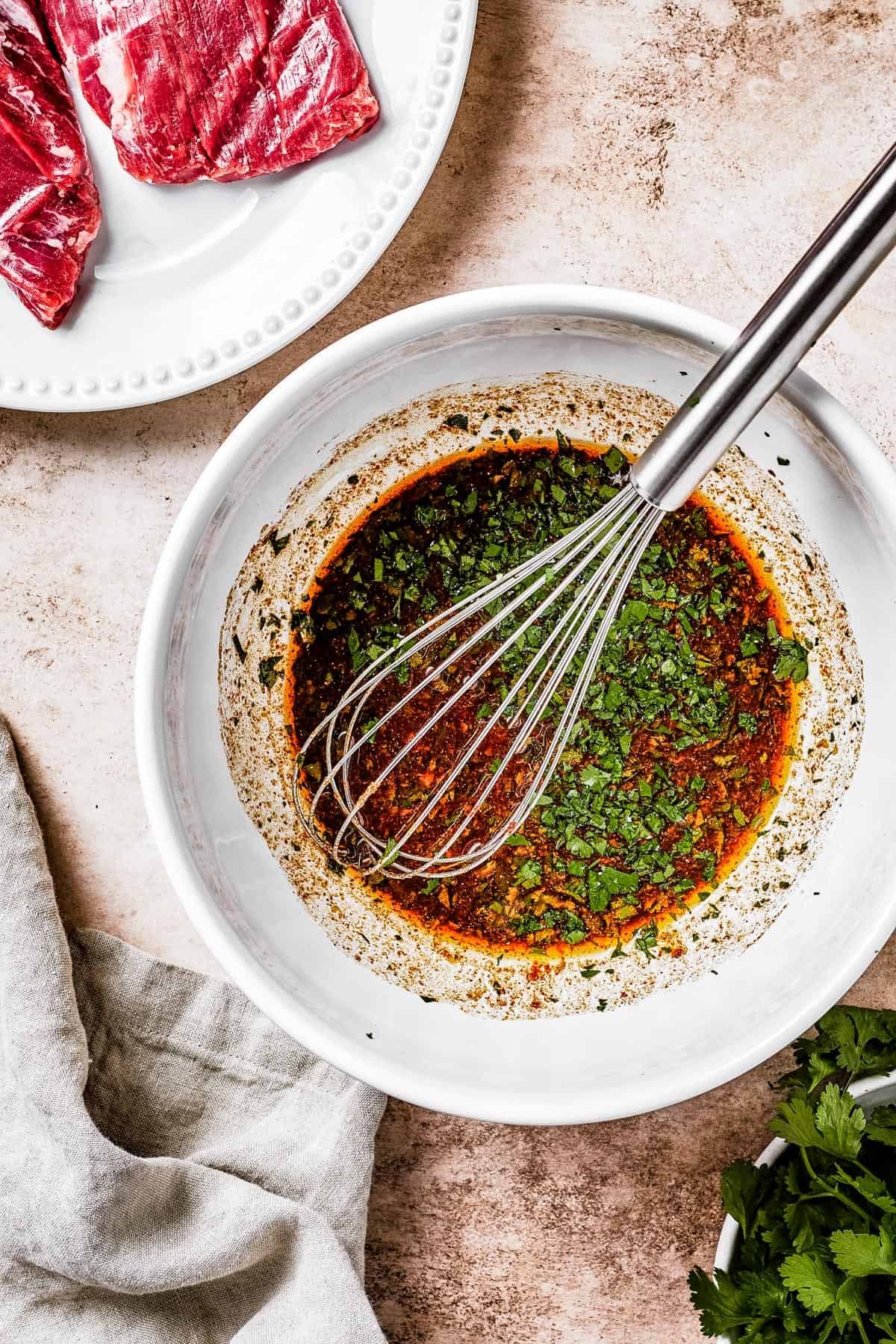 A white mixing bowl with dark-brown marinade and a whisk resting in it.