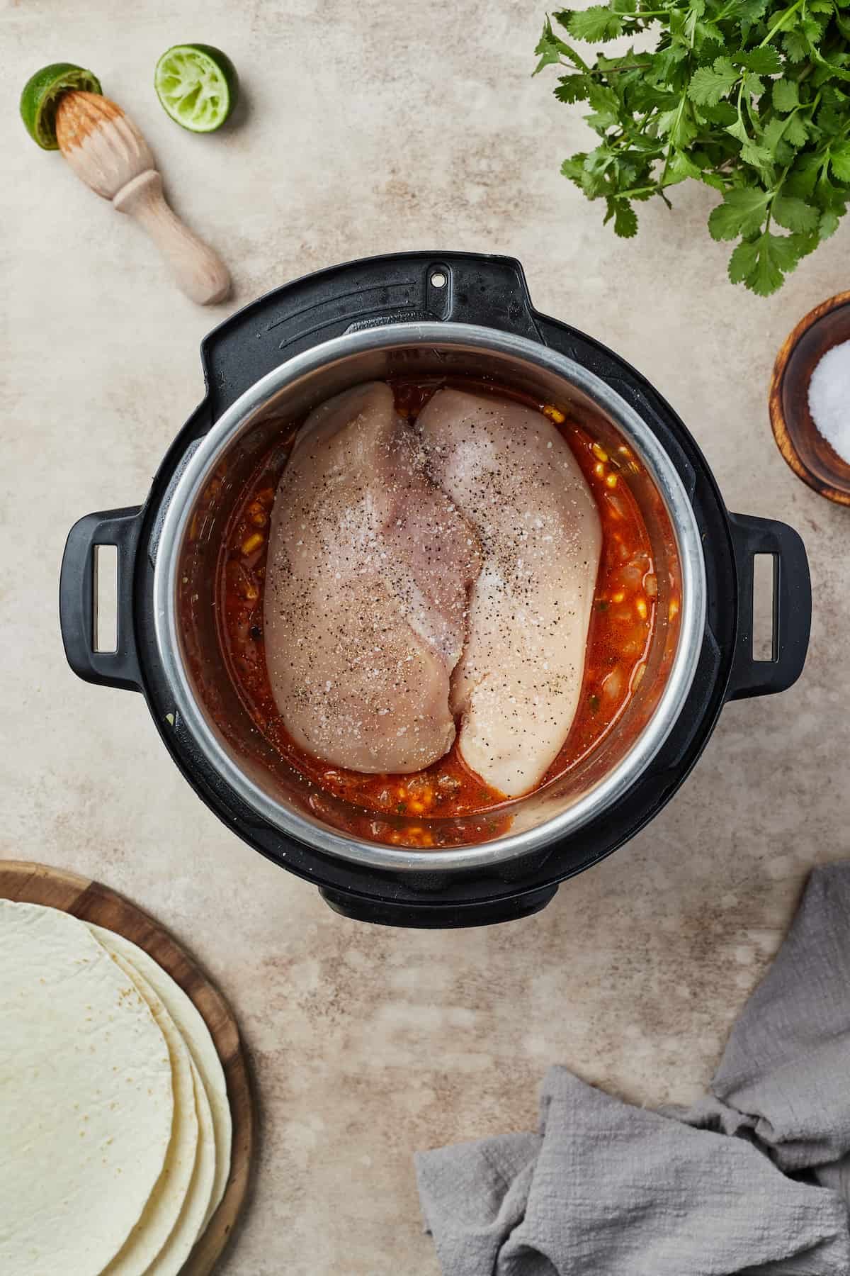 Uncooked chicken breast on top of a mixture of veggies and other ingredients in an Instant Pot.
