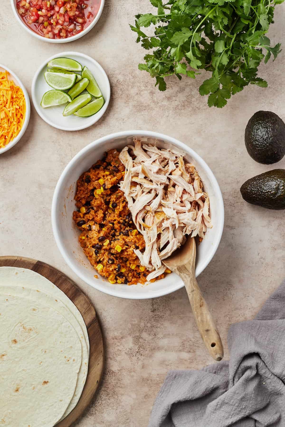 A white serving dish with cooked corn, beans, and other ingredients on one side, and shredded chicken on the other side. A wooden spoon is resting in the dish.