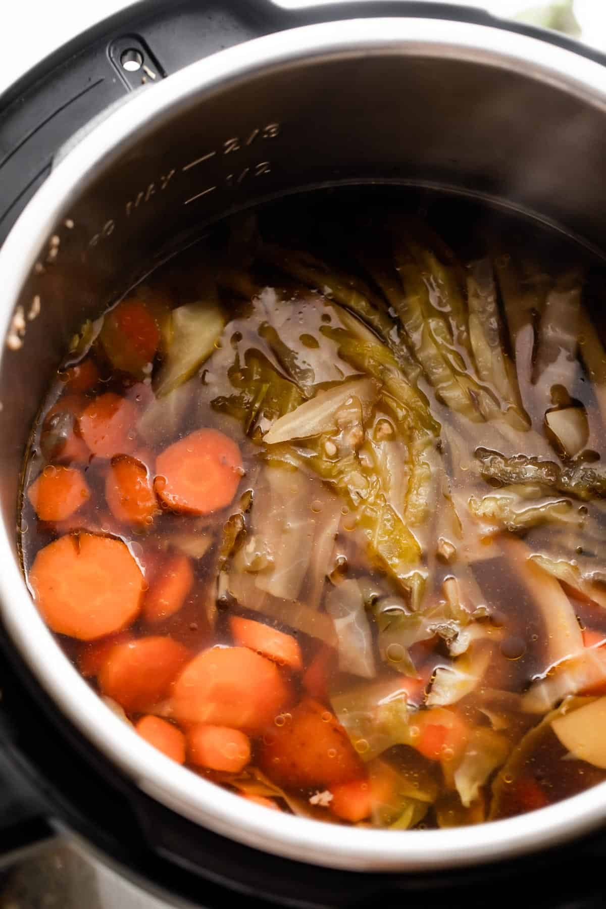 overhead shot of the insert of an instant pot filled with liquid, sliced carrots, cut potatoes, and sliced cabbage.