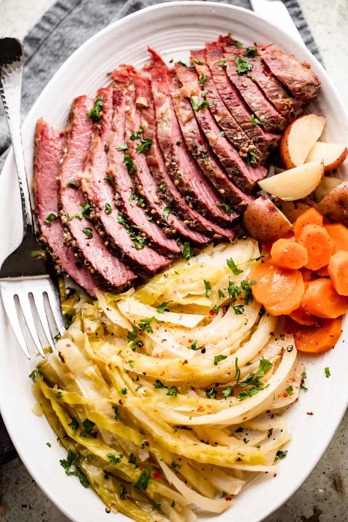 sliced instant pot corned beef, cabbage, carrots, and potatoes arranged on an oval serving platter.