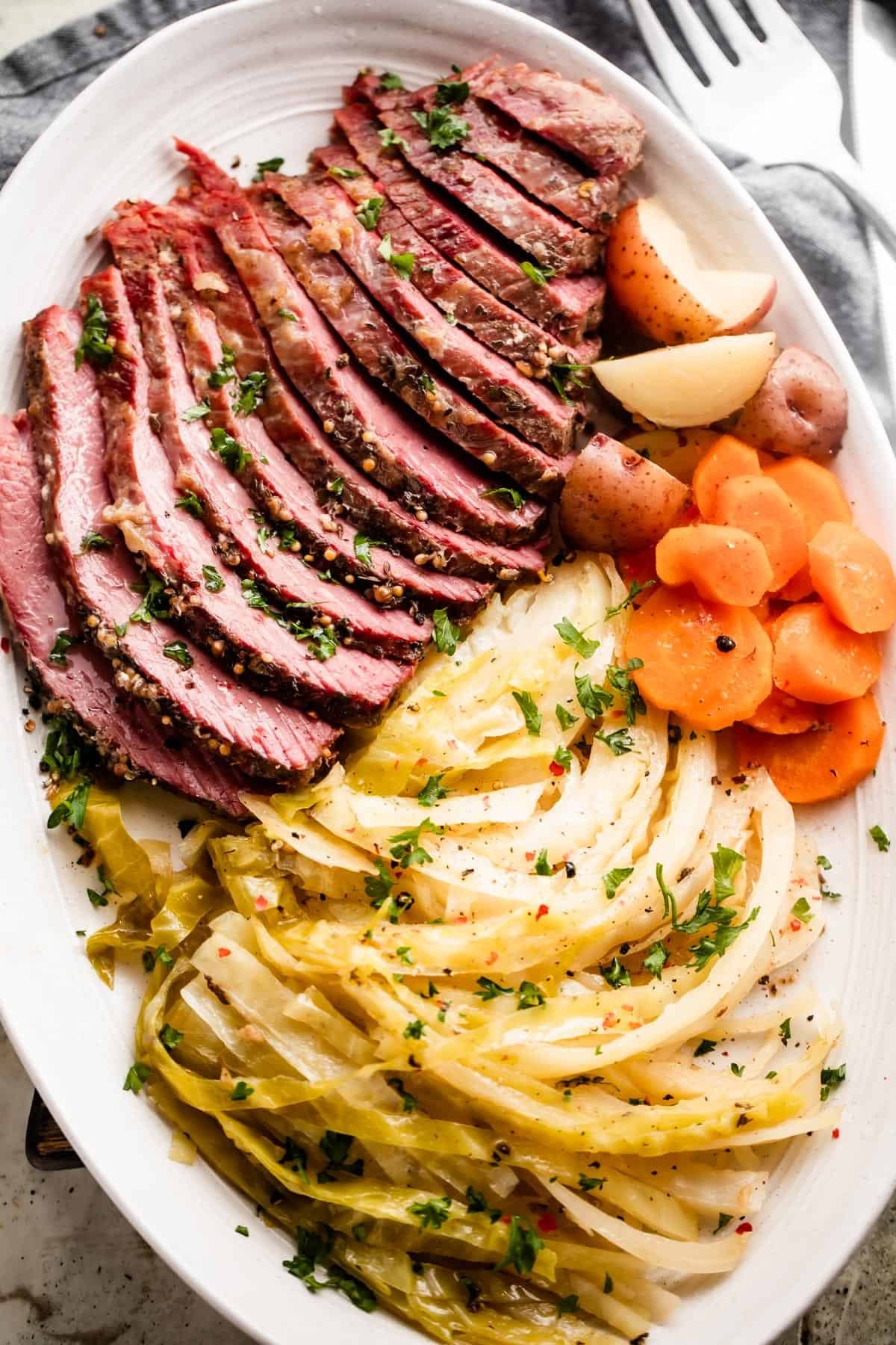 sliced instant pot corned beef, cabbage, carrots, and potatoes arranged on an oval serving platter.
