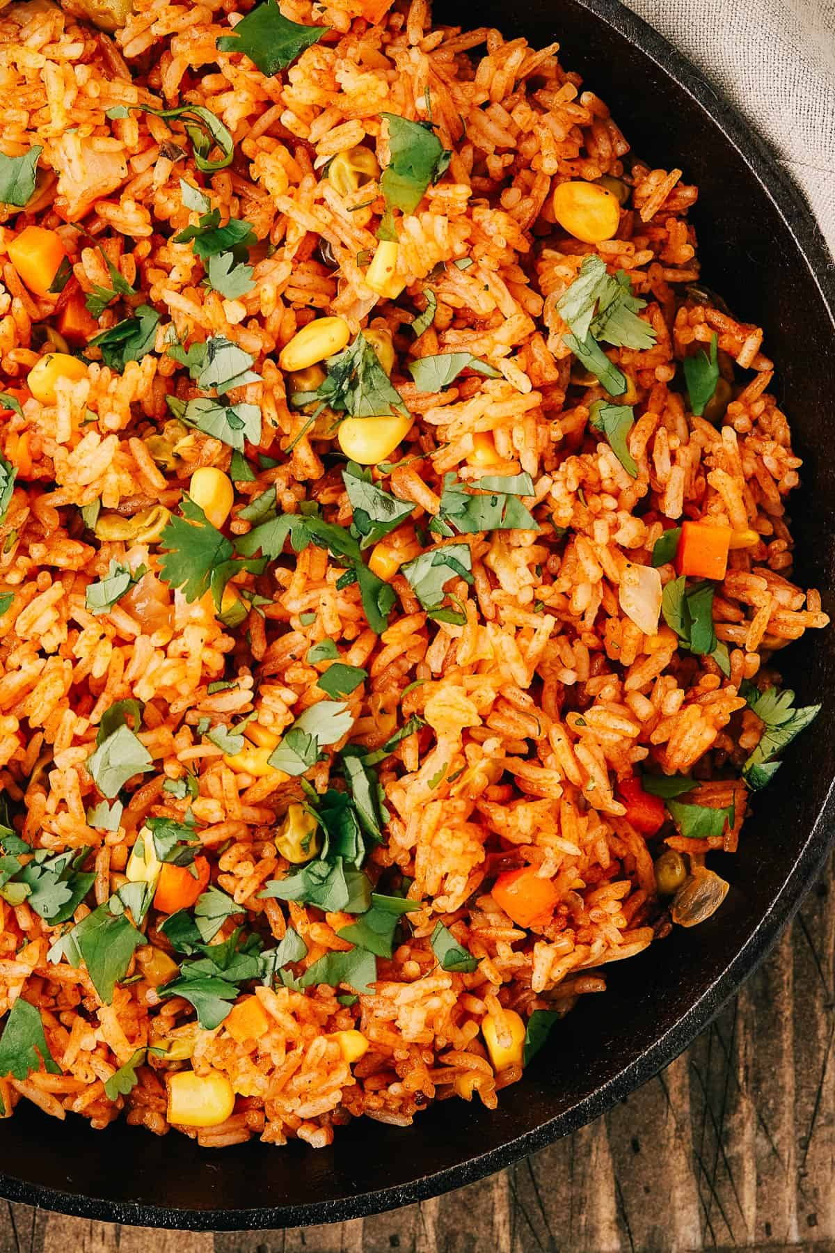 Close-up shot of a pan of seasoned rice and vegetables, garnished with fresh herbs.
