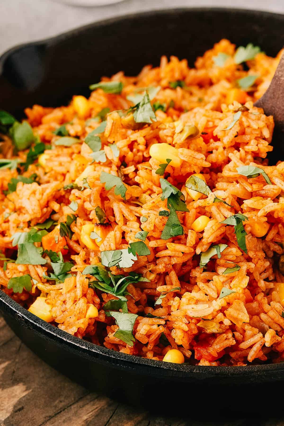 Side view of Mexican rice in a cast iron skillet, with a wooden utensil in the pan.