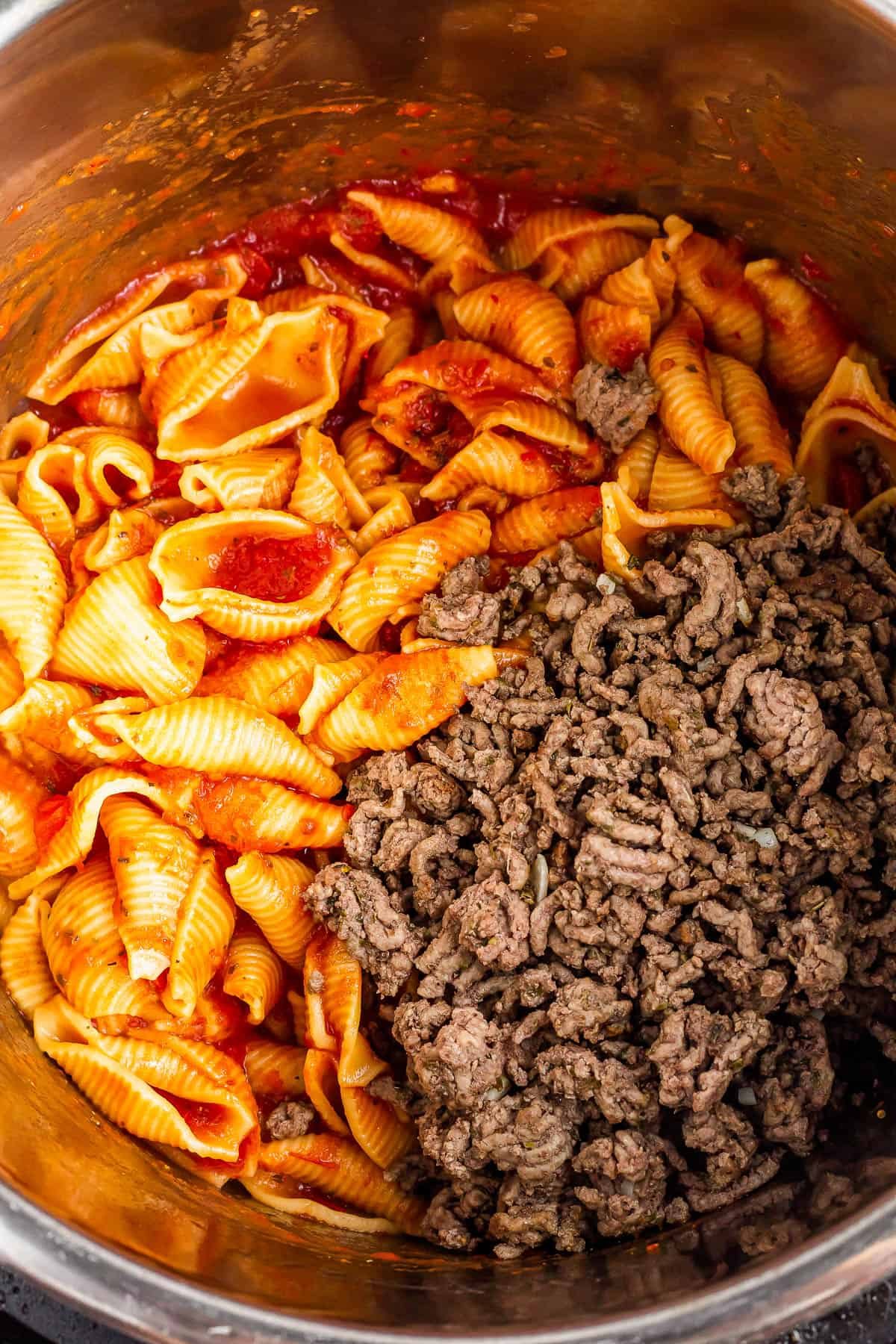 An overhead shot of an Instant Pot with cooked shells in sauce inside and a batch of browned ground beef added.