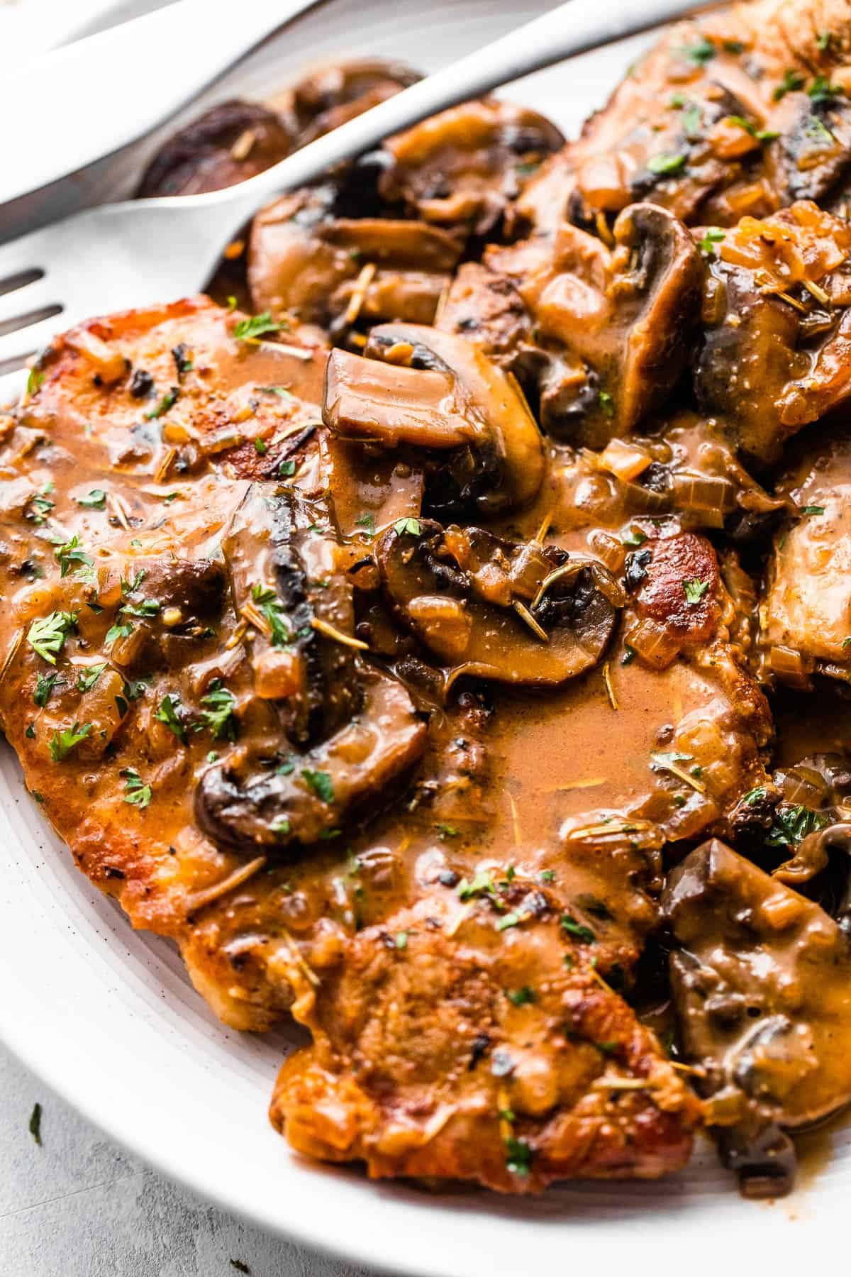 two bone in pork chops served on a white plate and topped with creamy mushroom gravy