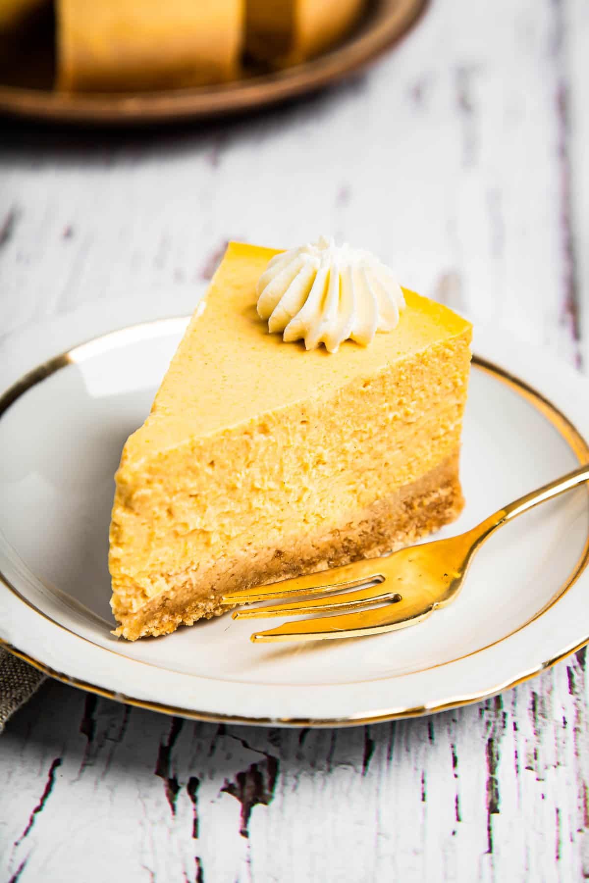 A slice of pumpkin cheesecake with a golden fork on a saucer.