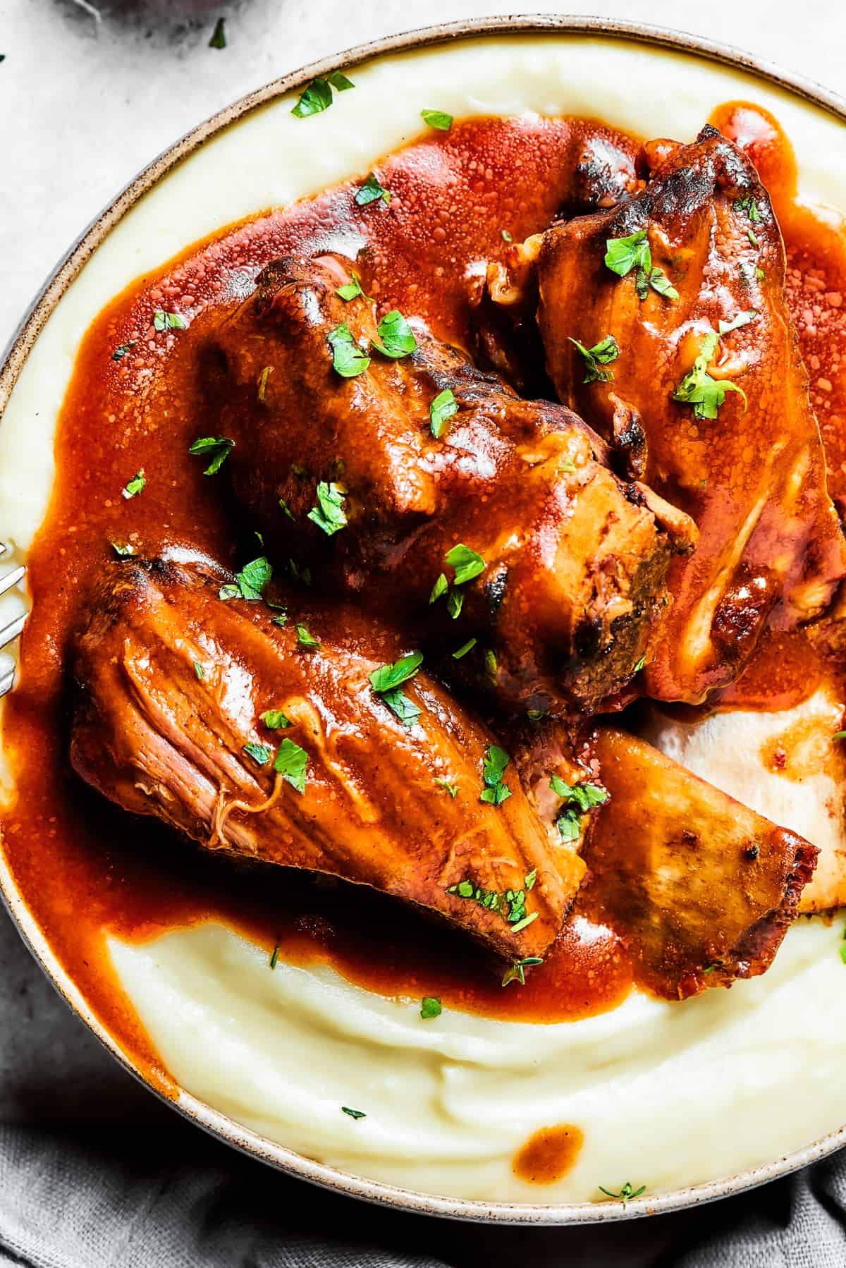 Close-up of Instant Pot short ribs topped with sauce and arranged atop mashed potatoes.