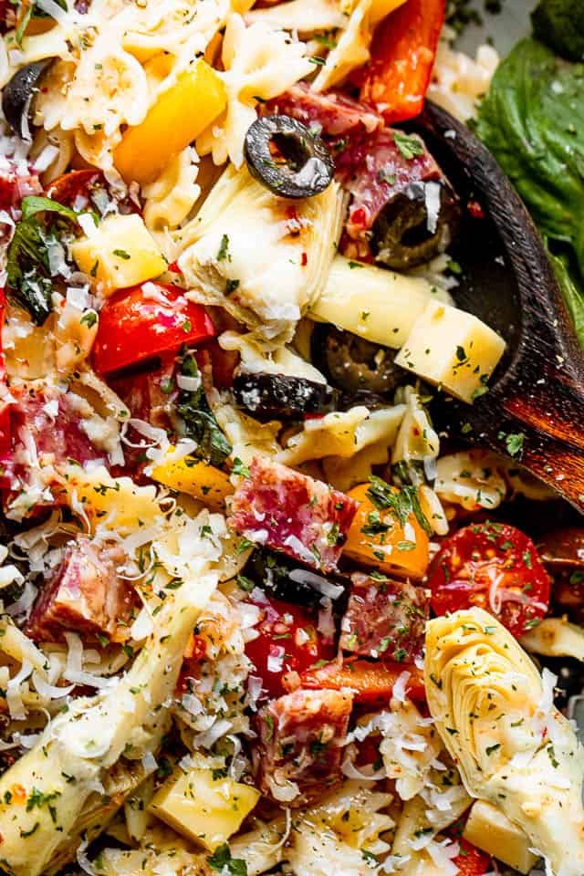 close up shotclose up shot of a salad bowl filled with pasta, cheese cubes, salami cubes, tomatoes, and olives