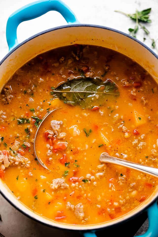 Butternut squash soup with Italian sausage soup in a Dutch oven with a ladle inside the soup.
