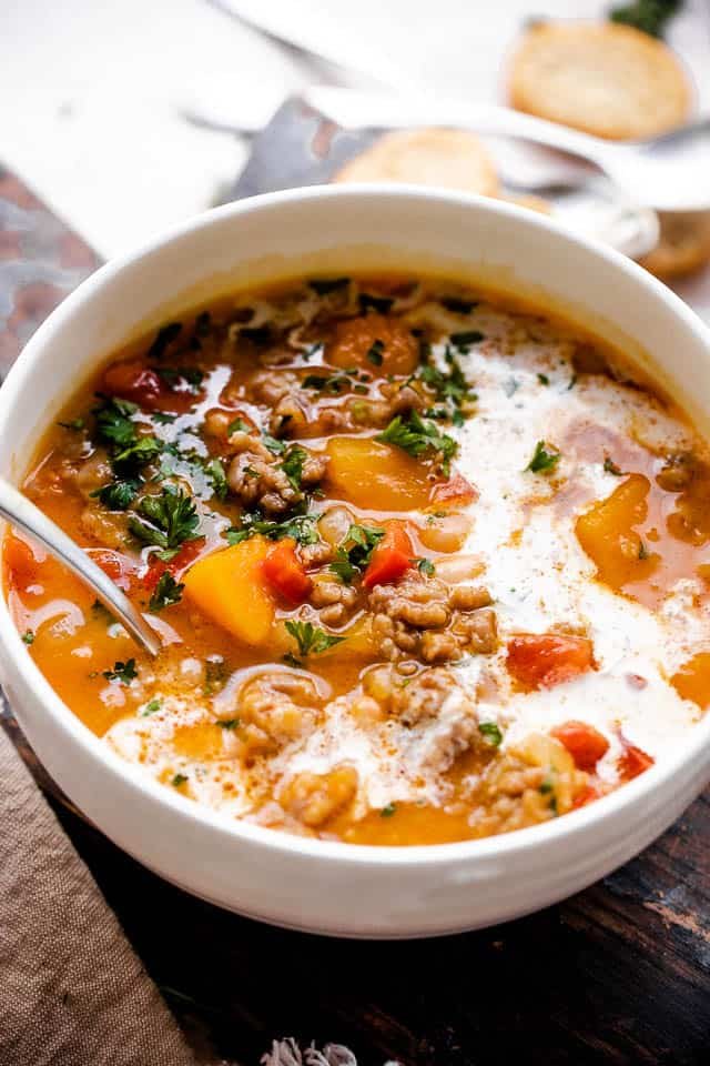 Side shot of butternut squash and sausage soup with cream in a white soup bowl.