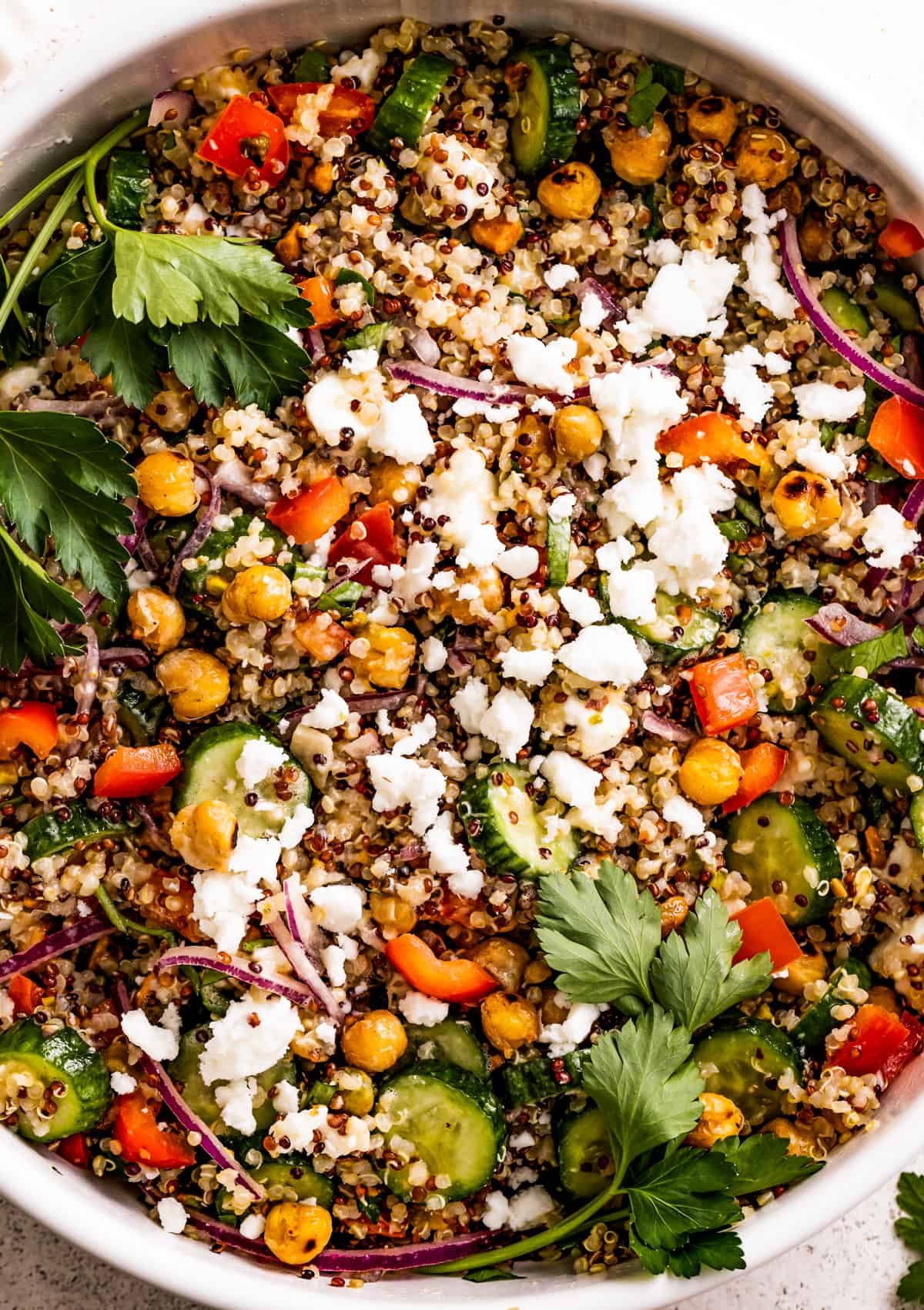 Close up shot of a salad with chickpeas, sliced cucumbers, red onions, peppers, herbs, and feta.