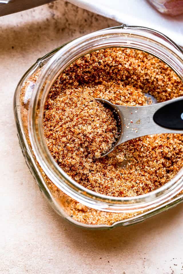a silver tablespoon inside a pork seasoning rub set in a glass jar