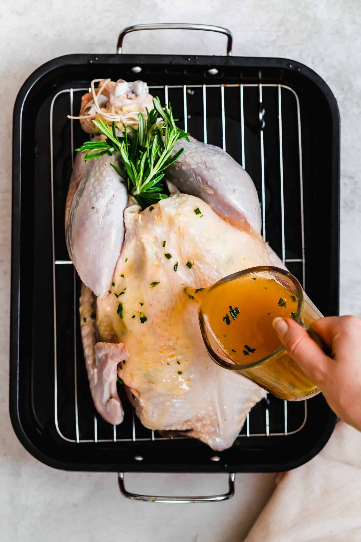 Uncooked turkey in a pan with broth being poured on top.