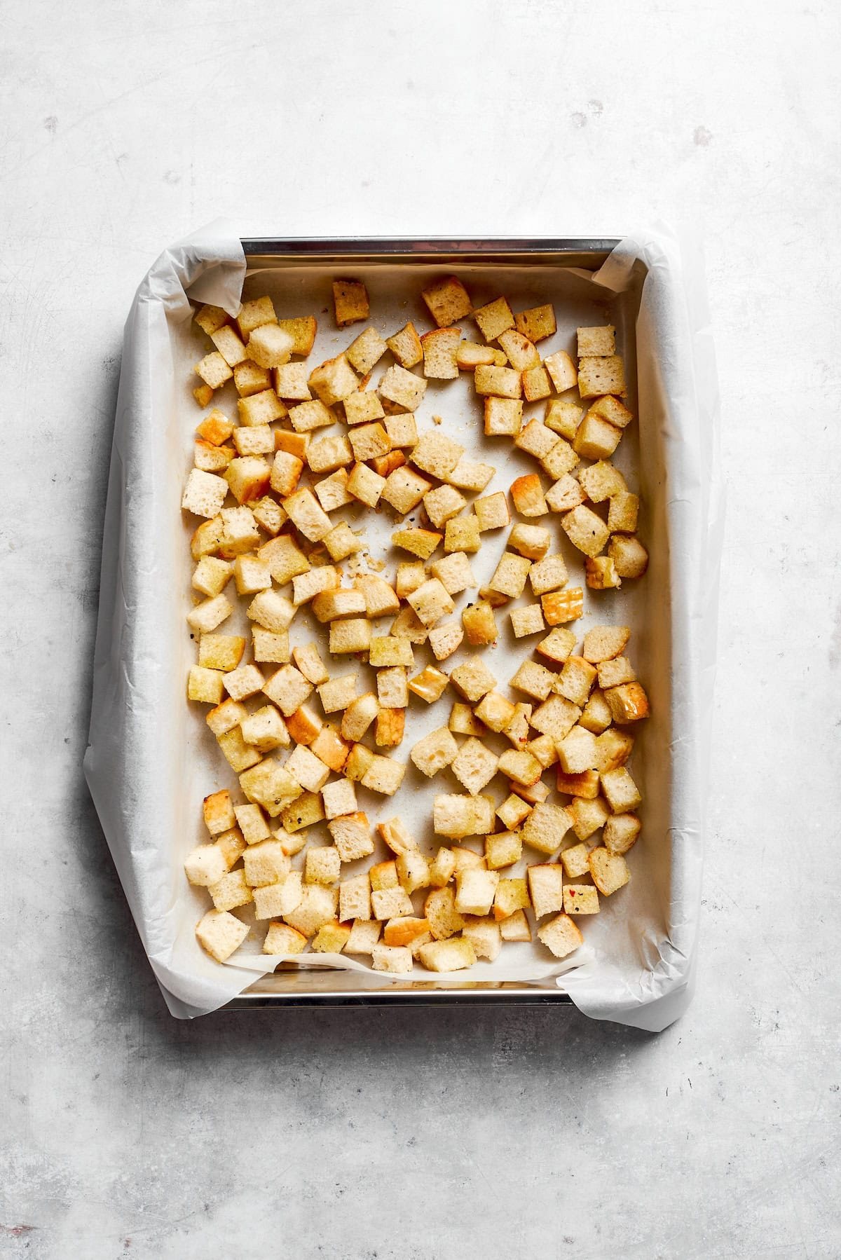 Homemade croutons cool on a lined baking sheet.