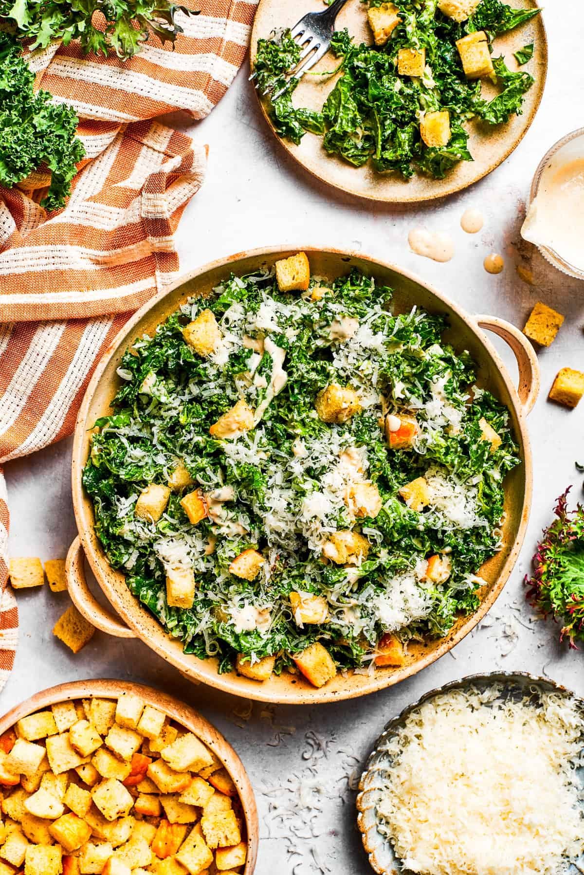 A large bowl of kale Caesar salad garnished with homemade croutons and shredded cheese.