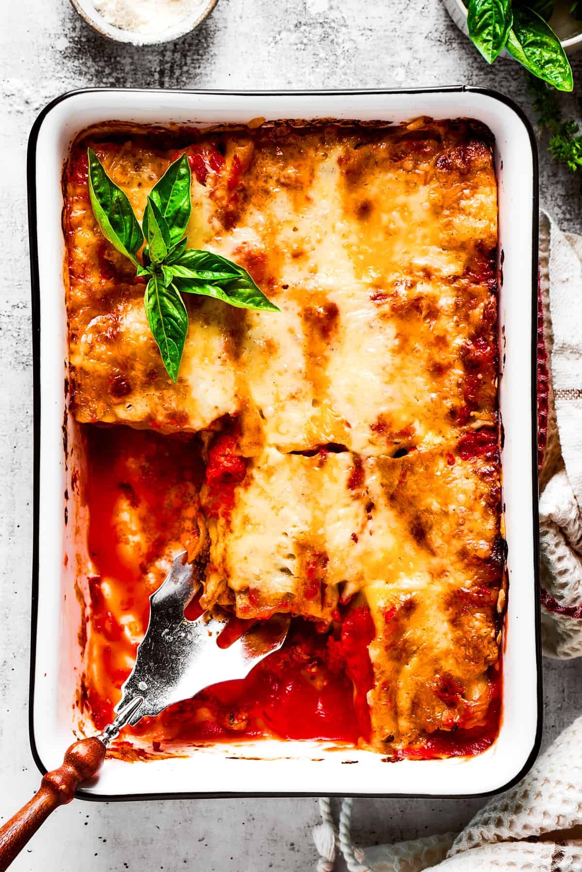 Overhead view of a baking dish filled with lasagna roll ups with a few removed, and a serving spoon removing a roll.