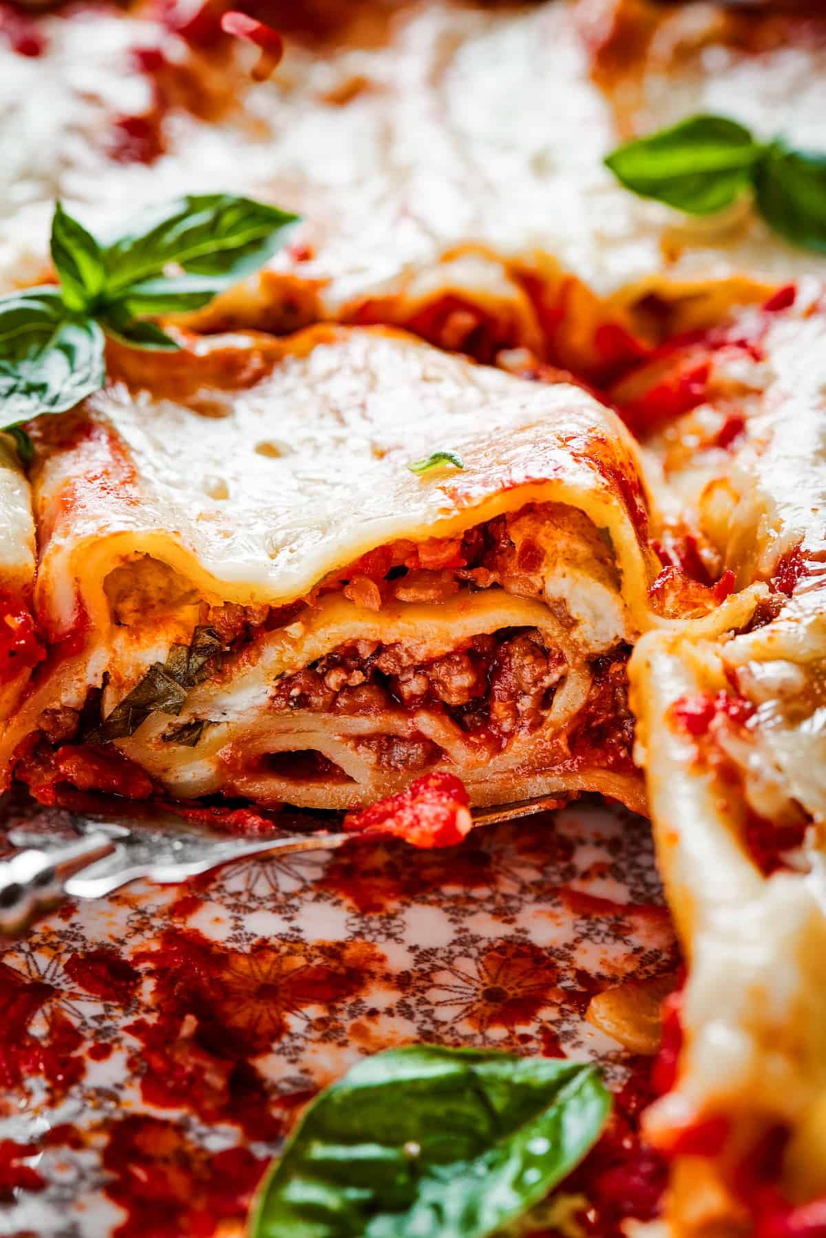 Close up of a lasagna roll up on a plate topped with basil.