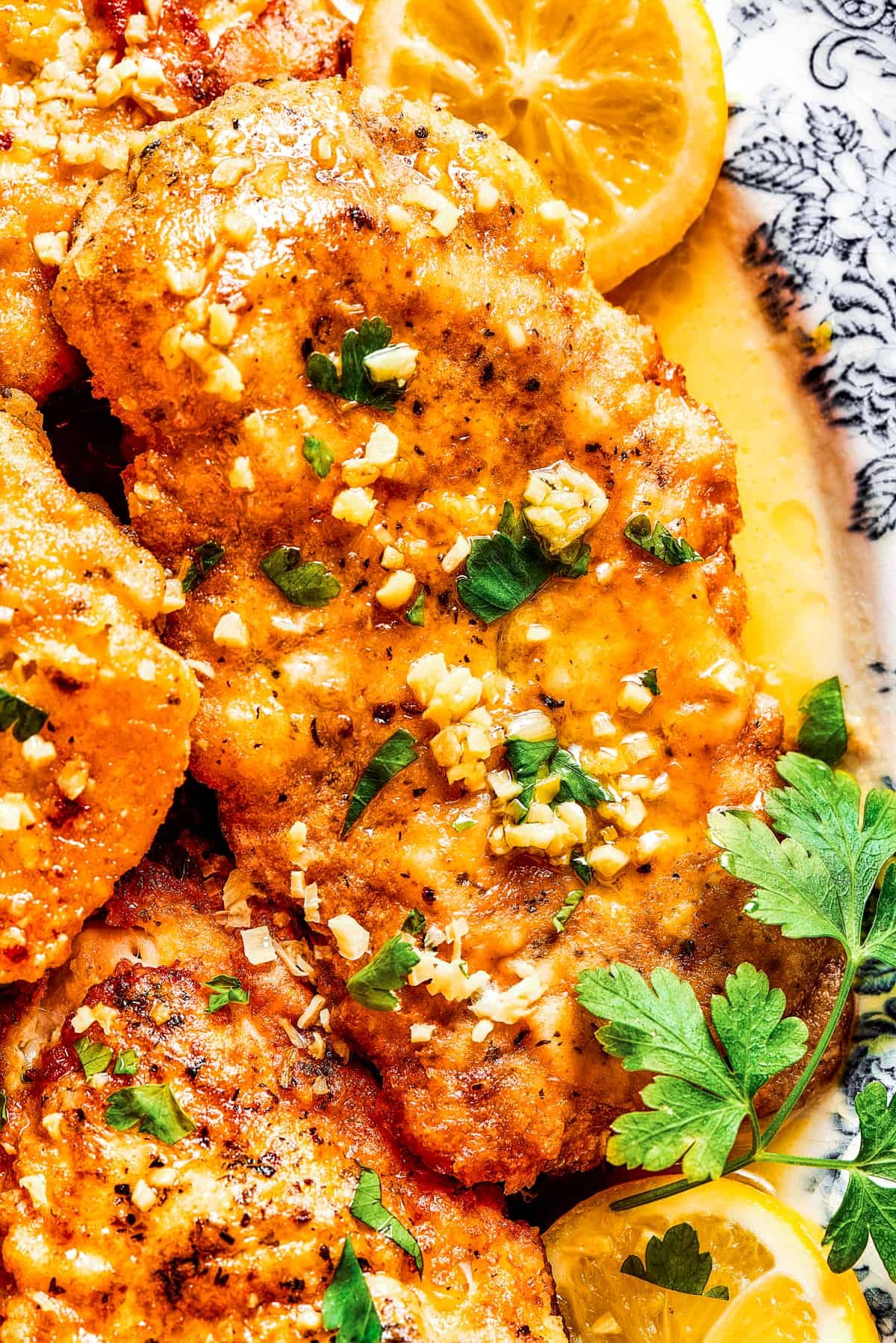 Close-up shot of lemon chicken breast on a platter, with garnishes of lemon.