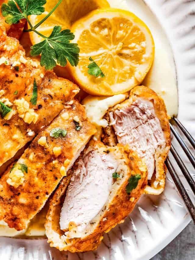 Sliced Breaded chicken with parsley and lemon slices placed next to it.