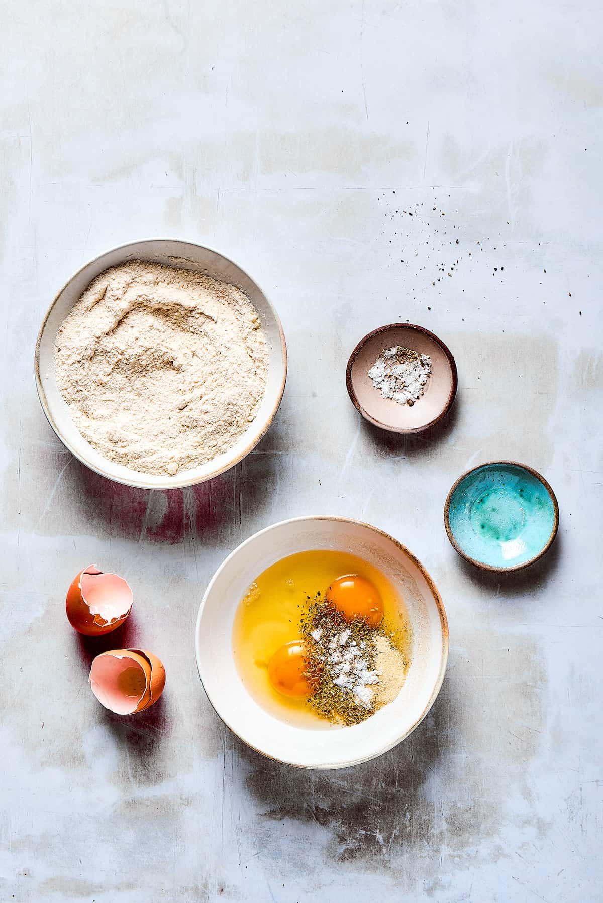A bowl of breading ingredients next to a bowl of beaten eggs and seasonings.