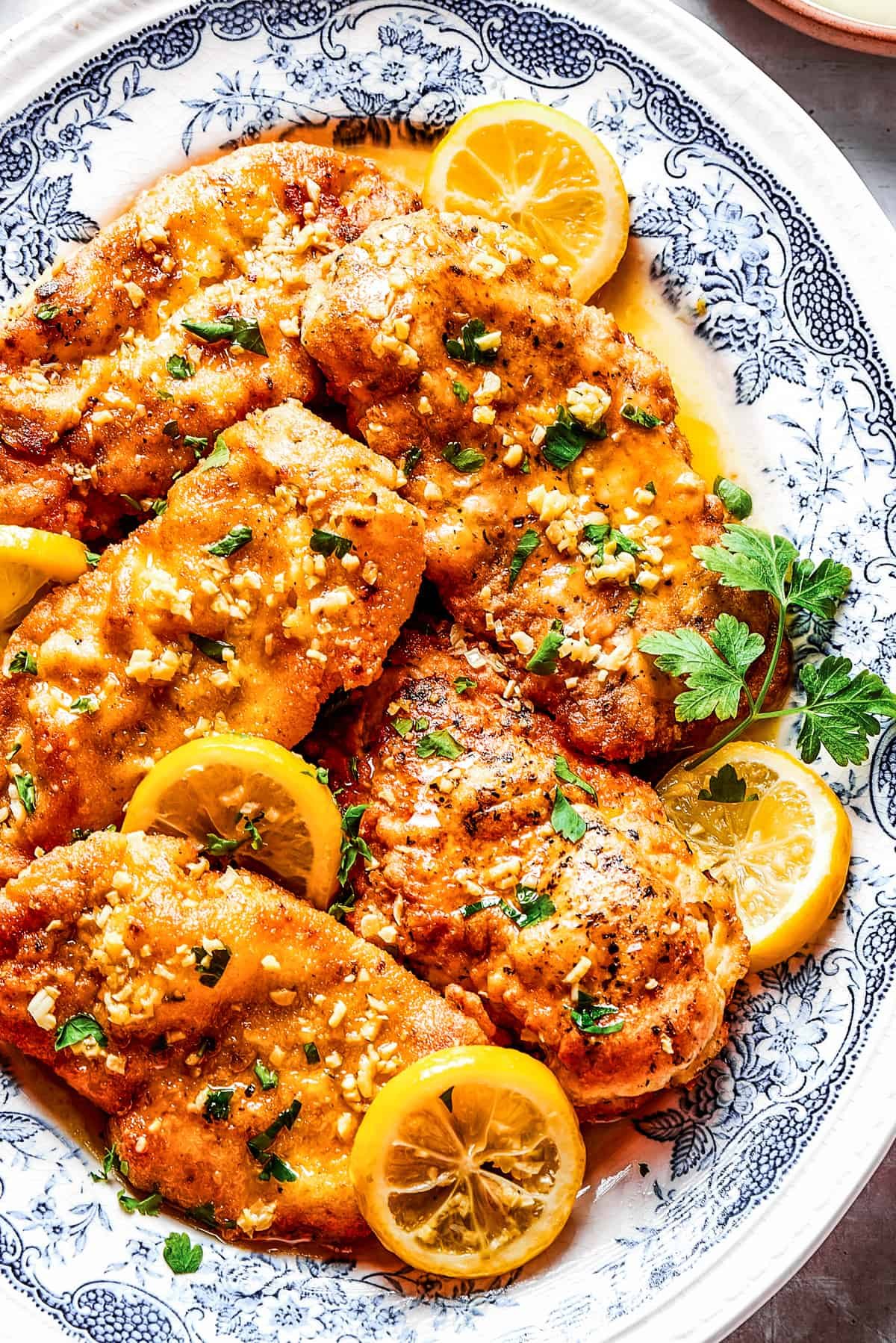 Homemade lemon chicken recipe arranged on a platter with parsley and lemon slices.