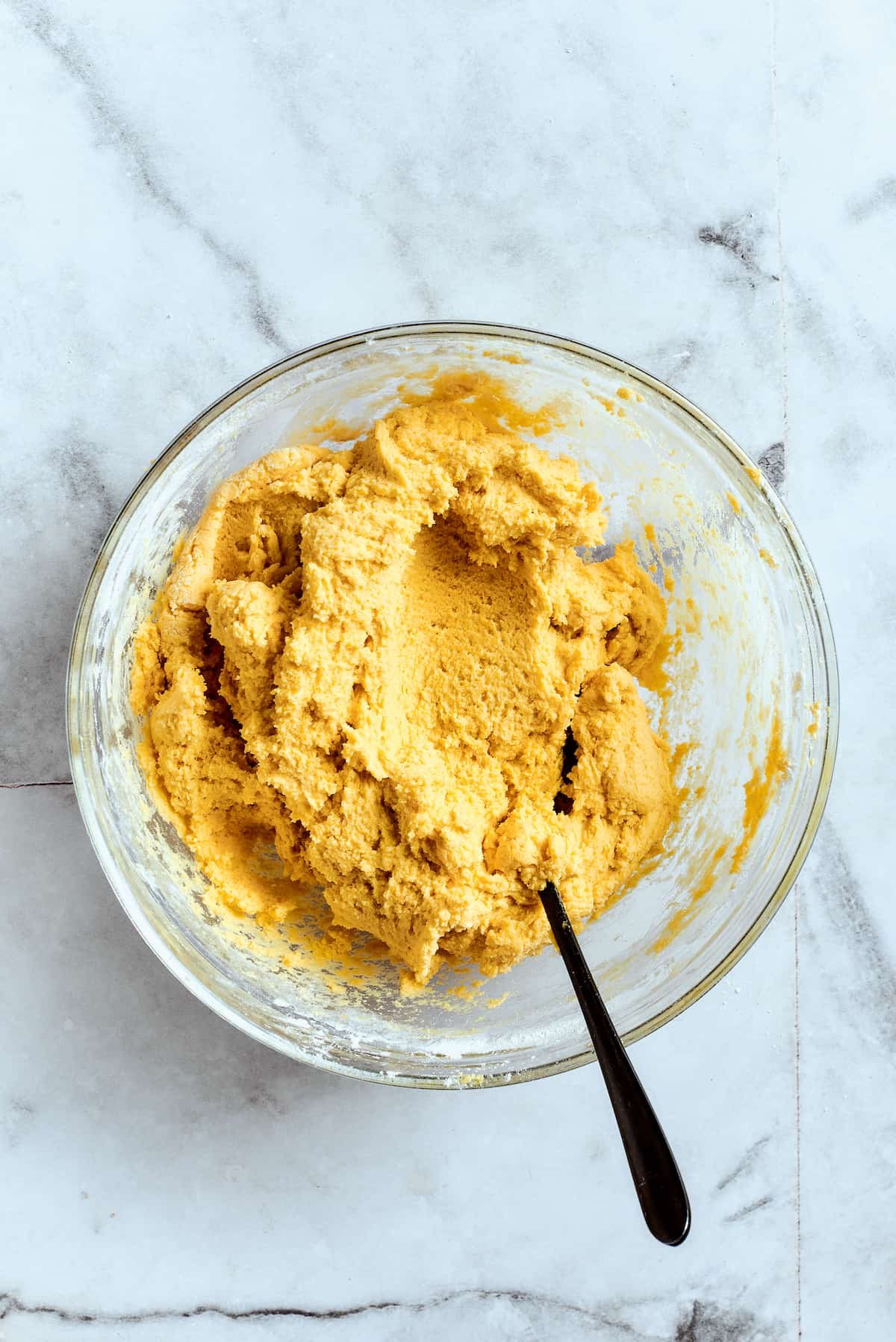 Overhead view of a mixing bowl filled with lemon cookie dough and a spoon.