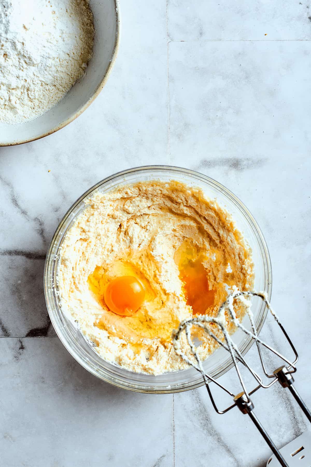 Overhead view of a mixing bowl with creamed butter and two eggs on top, with beaters.