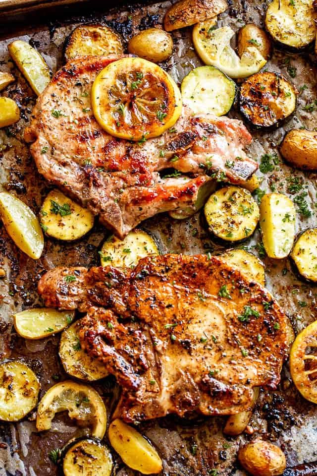sheet pan with baked pork chops on top of slices of squash and lemons