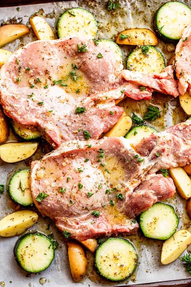baking sheet with raw pork chops set on top of squash slices