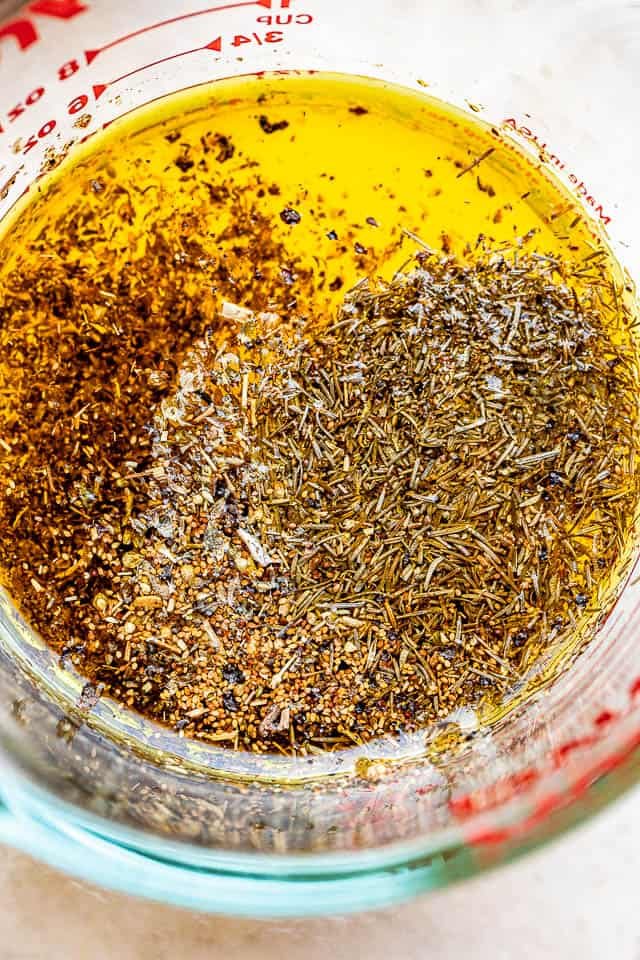 glass measuring cup filled with lemon dressing mixture with dried herbs