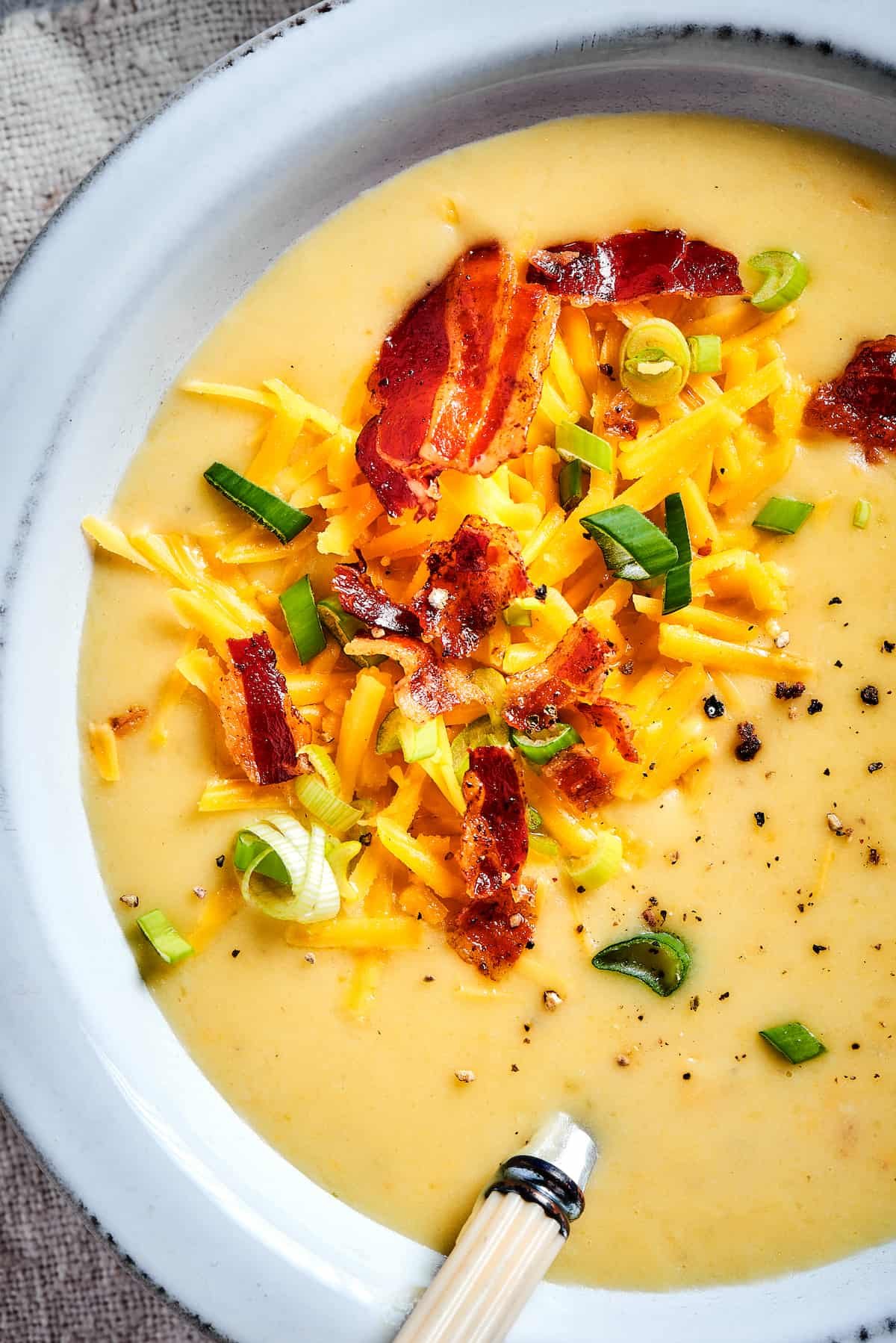 Close-up shot of bacon, green onions, and cheese sprinkled into a bowl of creamy soup.
