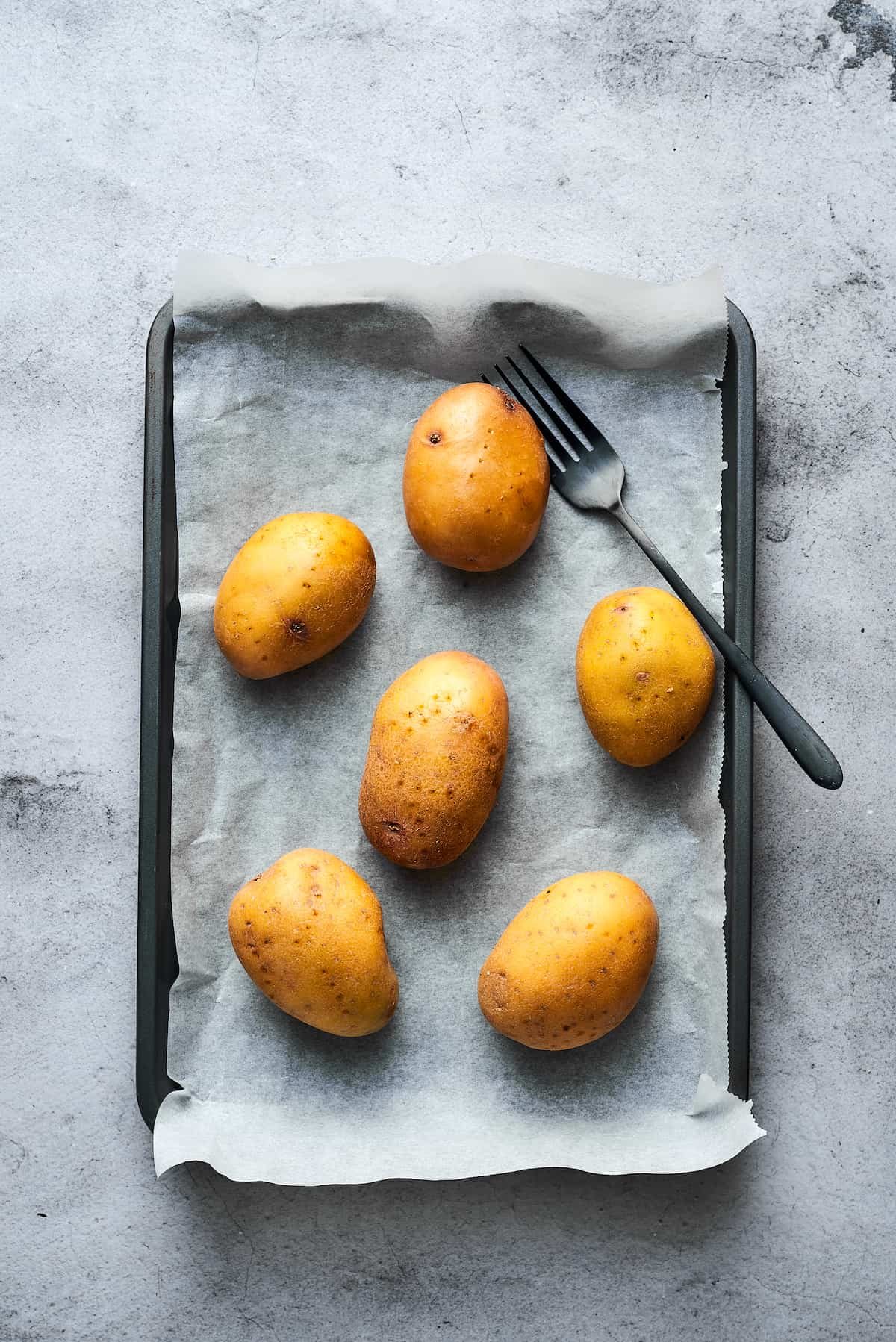 Potatoes washed, pricked with a fork, and arranged on a baking sheet.