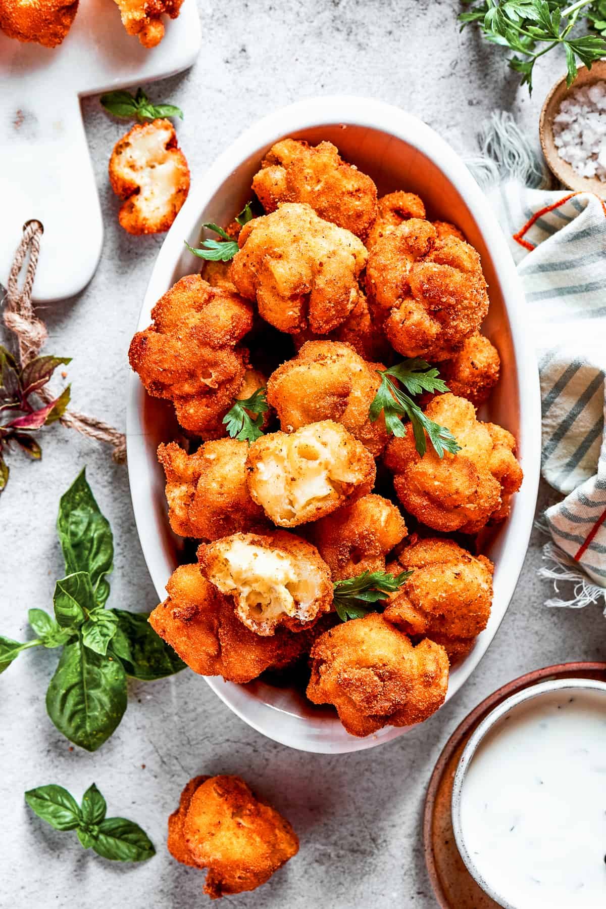 Overhead view of a serving bowl full of mac and cheese bites, next to more of them and garnished with fresh herbs.