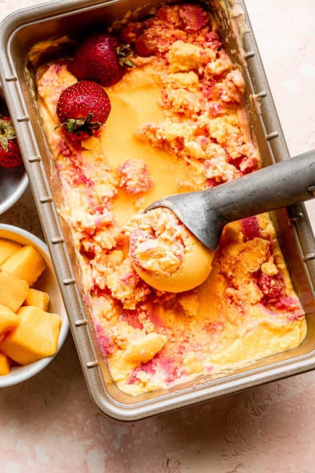 top shot of mango strawberry frozen yogurt in a loaf pan with ice cream scooper