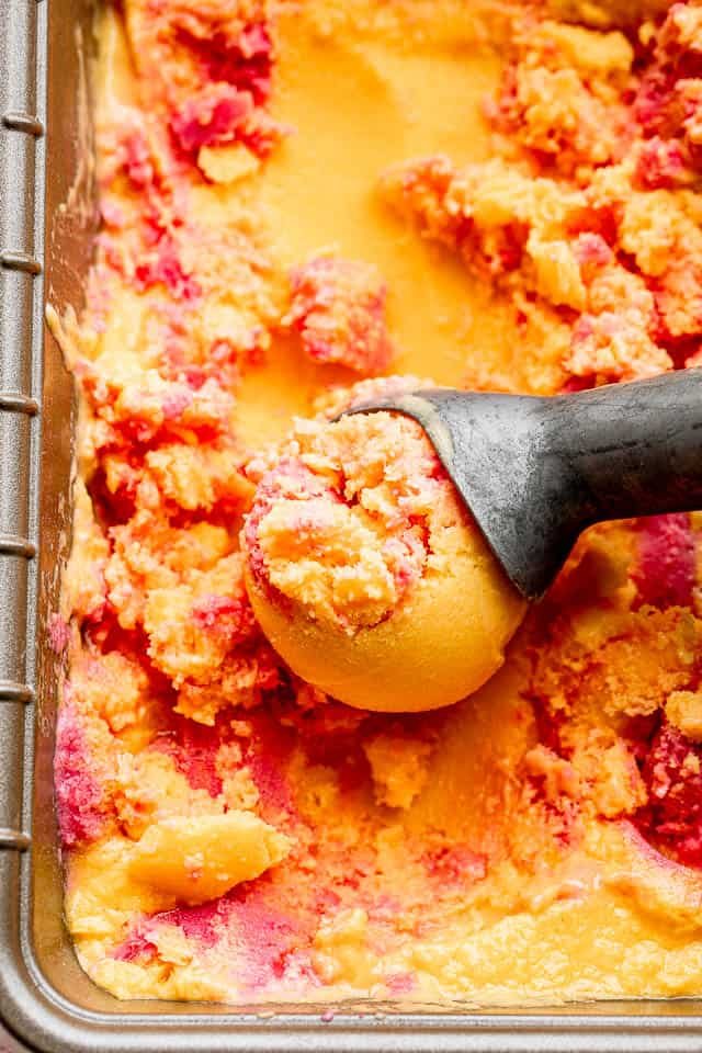 close up shot of mango strawberry frozen yogurt in a loaf pan with an ice cream scoop