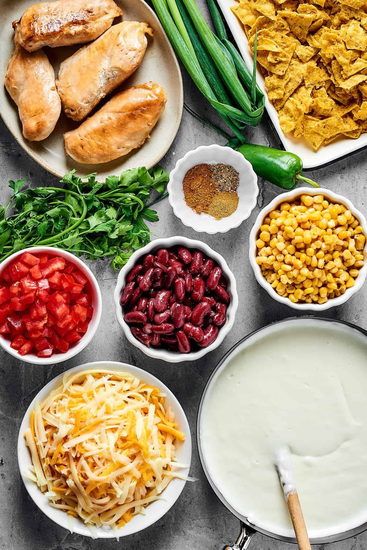 From top: Cooked chicken breast, green onions, crushed chips, seasonings, chopped tomatoes, beans, corn, cheese, white sauce.