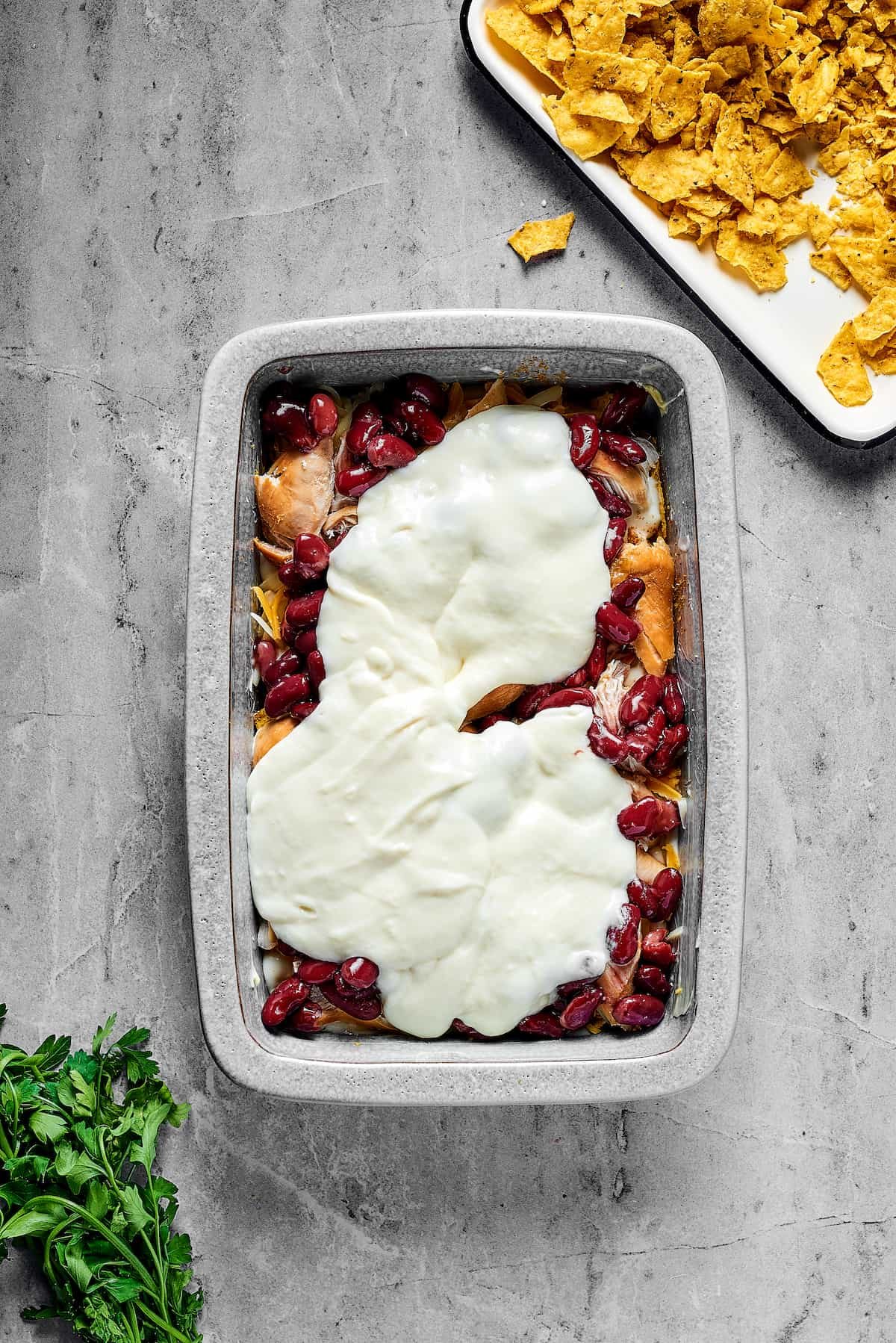 Beans, white sauce, chicken, and other ingredients layered in a rectangular pan.