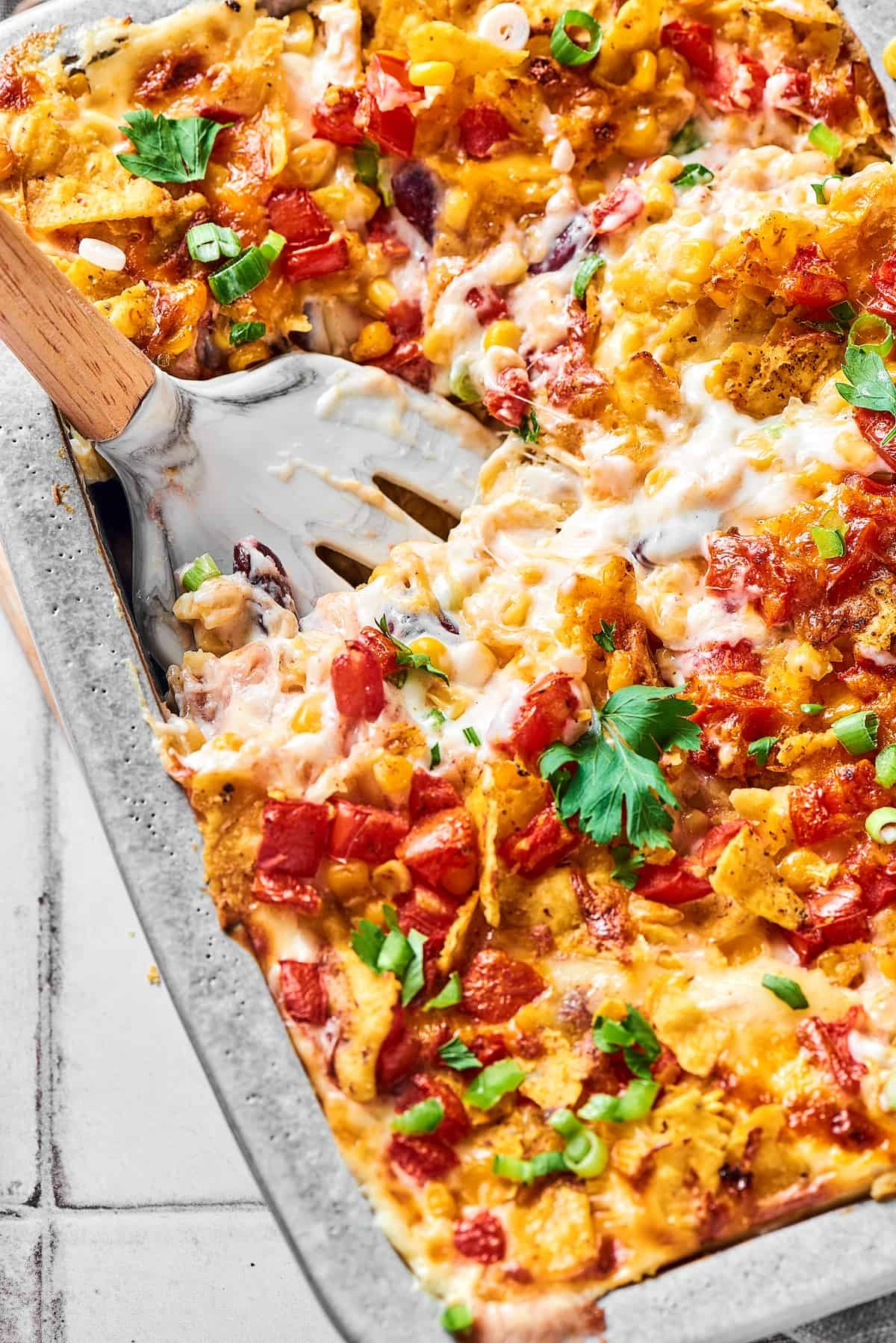 A serving utensil in a large baking pan of cheesy chicken bake.