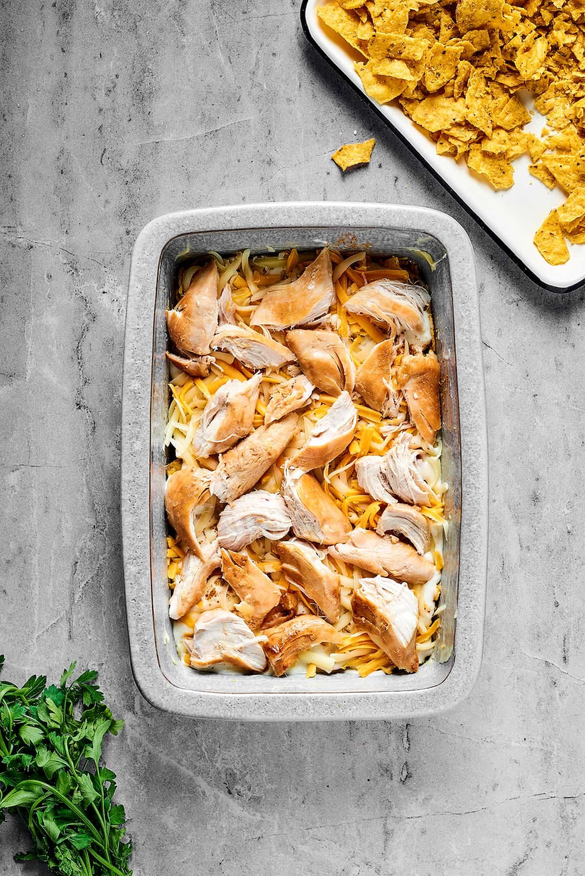 Cheese and chicken layered over other ingredients in a baking dish.