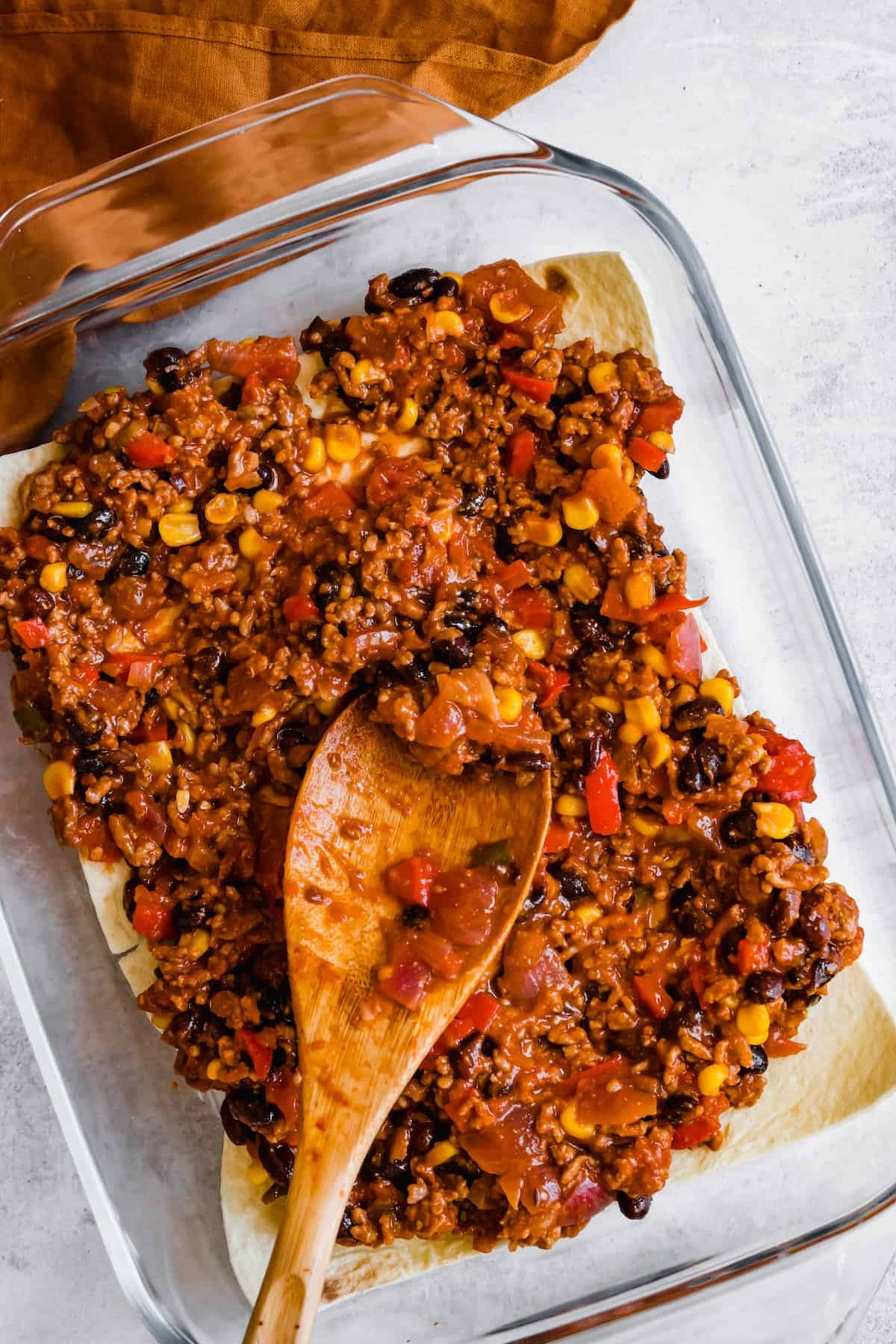 A Wooden Spoon Spreading a Layer of Lasagna Filling Over a Layer of Tortillas