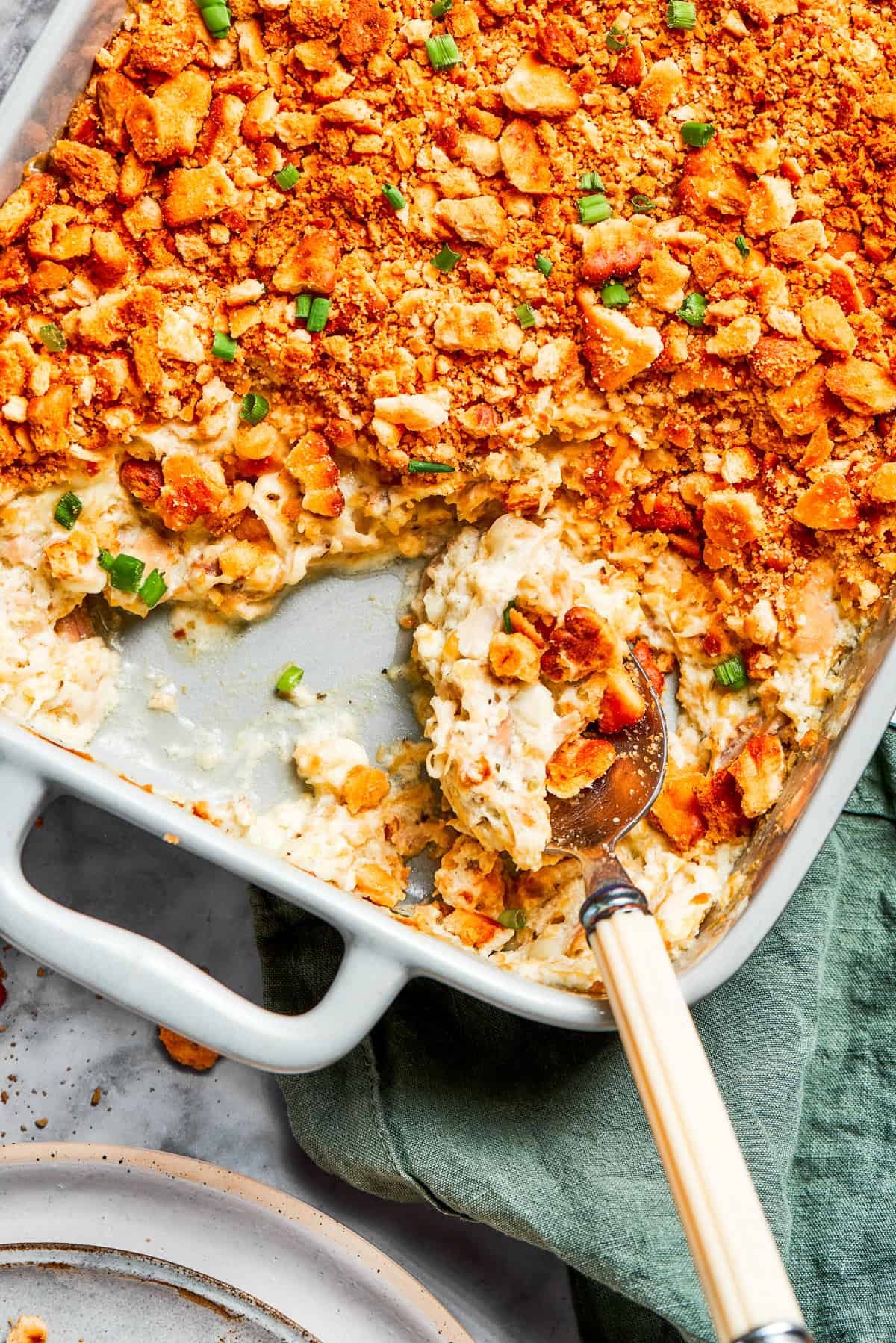 A serving spoon scooping out million dollar chicken casserole from a baking dish.