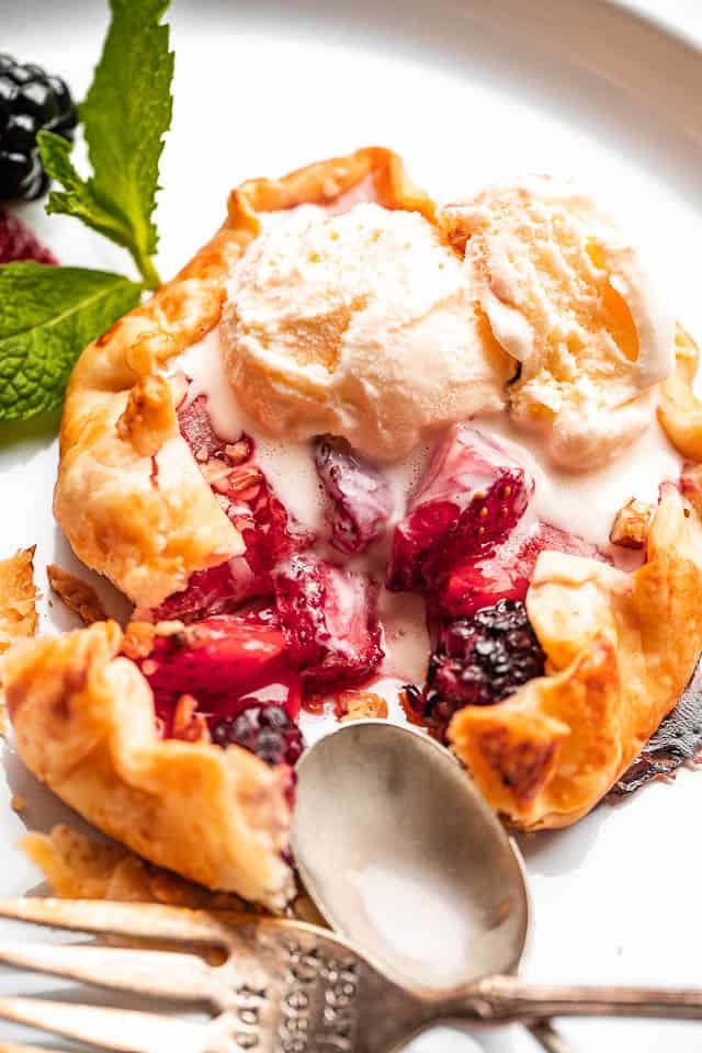 top view of an ice cream topped mini berry galette with a metal spoon and fork set on the side of it.