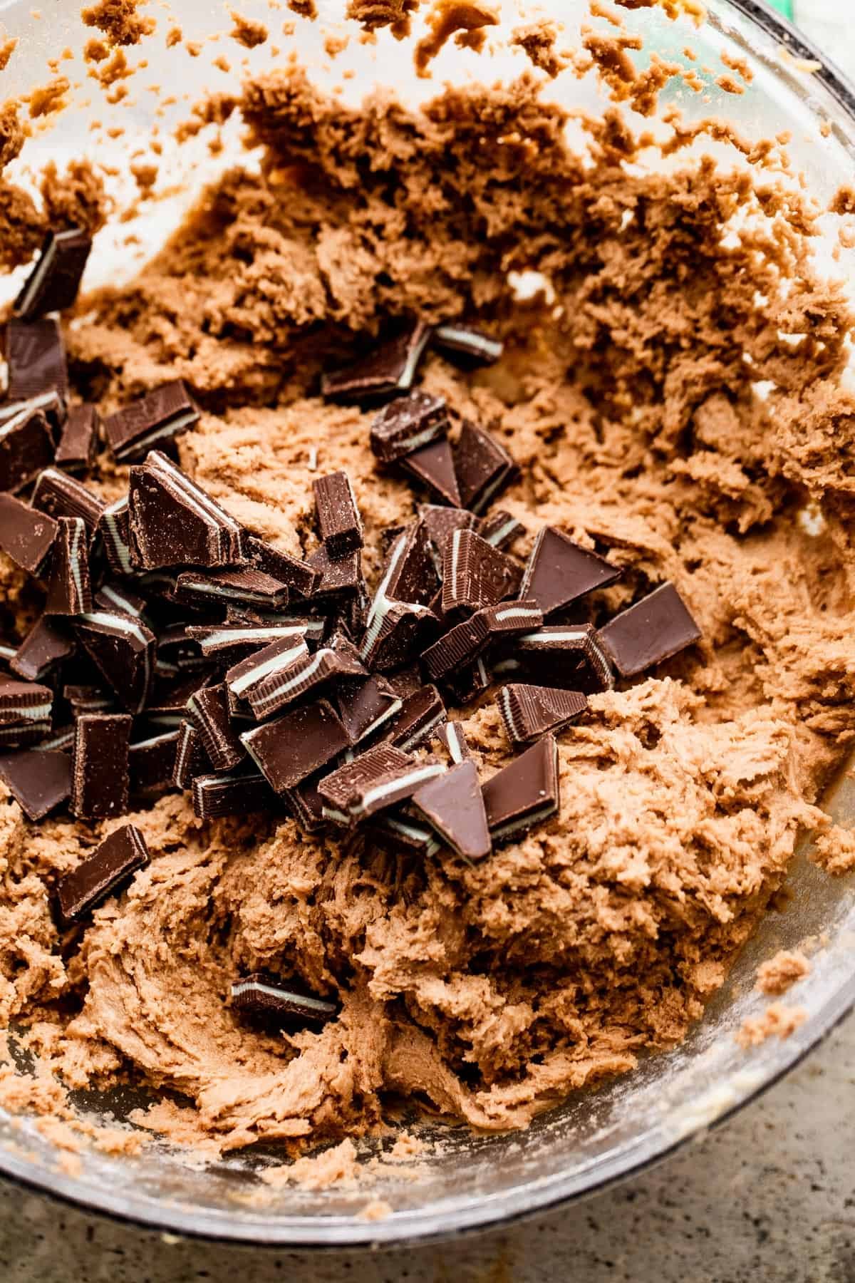 overhead shot of cookie dough in a mixing bowl with chopped chocolate mints in the center of the dough.