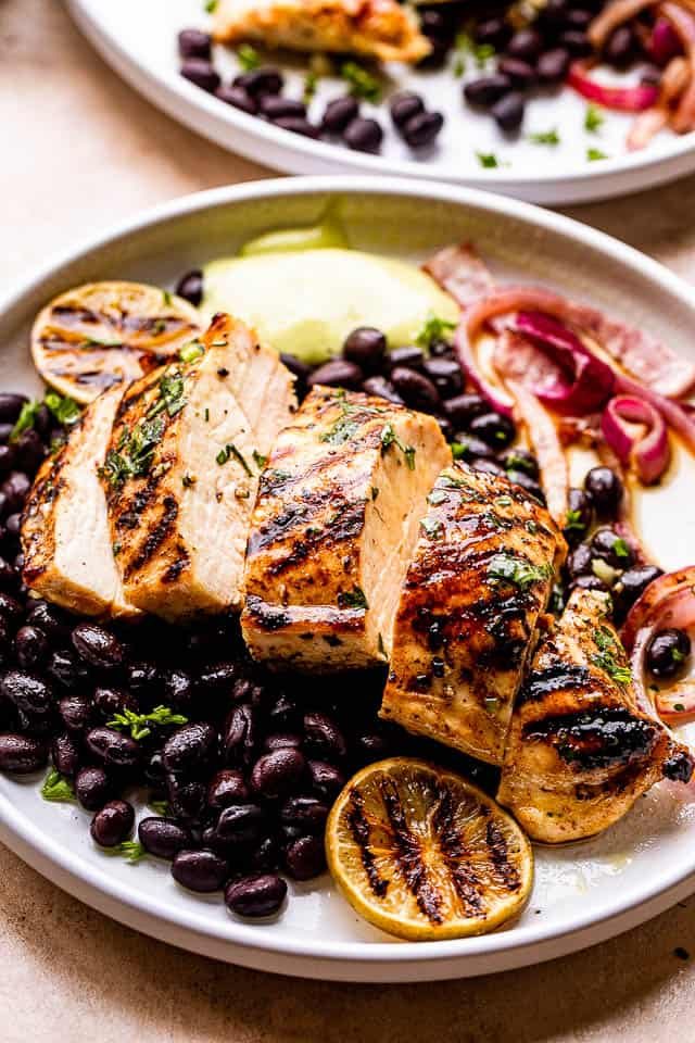 Grilled Mojo Chicken Breast cut in slices and served over black beans and guacamole to the side.